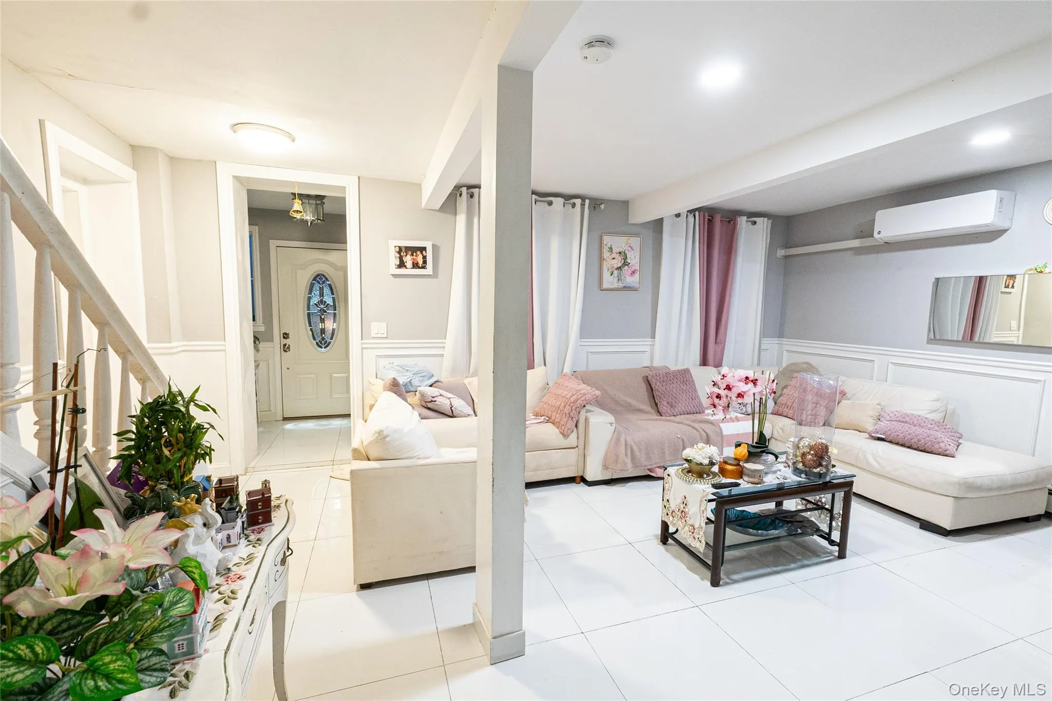 Living area with a decorative wall, a wainscoted wall, light tile patterned floors, a wall unit AC, and stairway Living area with a decorative wall, a wainscoted wall, light tile patterned floors, a wall unit AC, and stairway