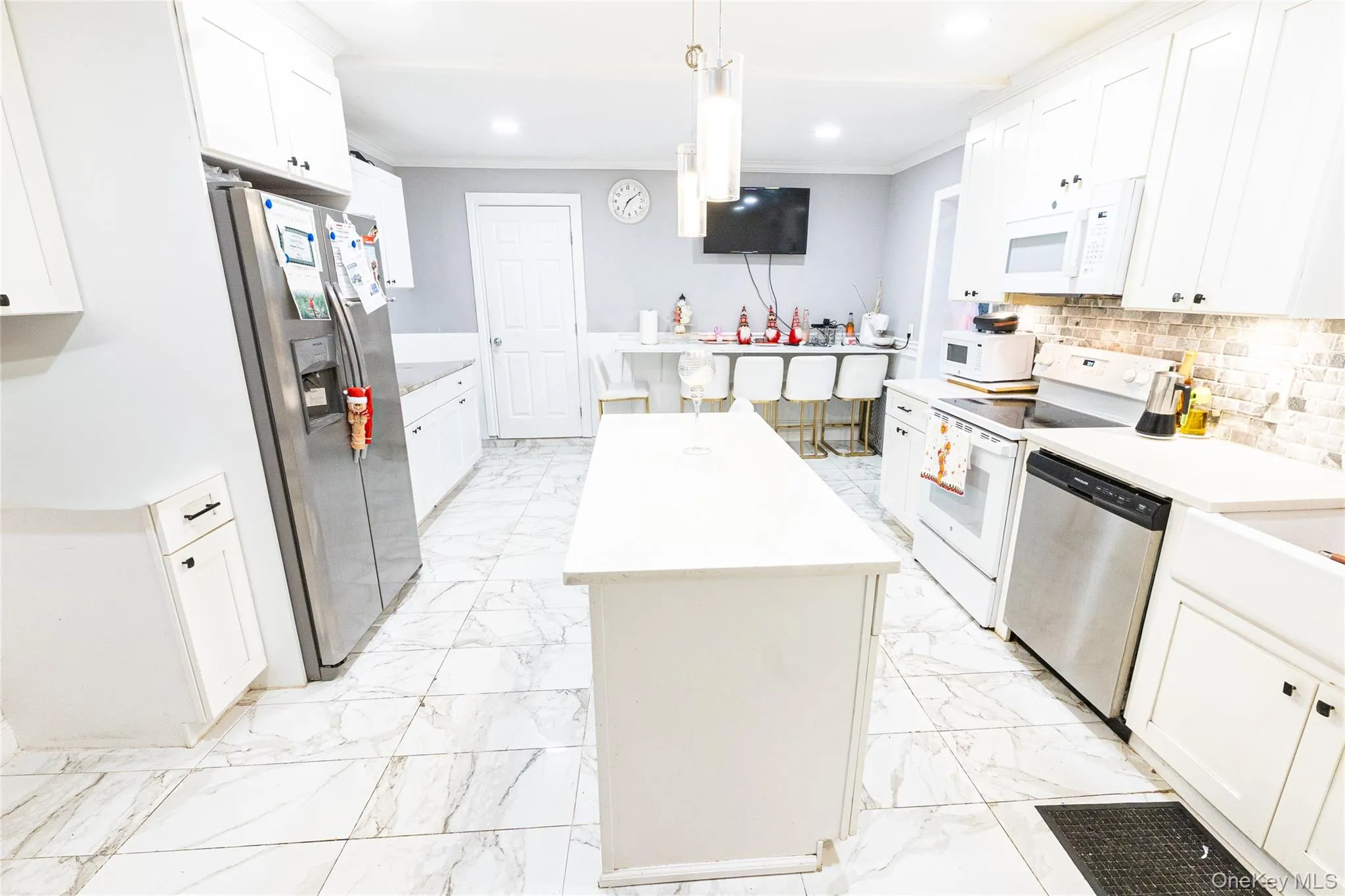 Kitchen with a kitchen island, stainless steel appliances, white cabinetry, hanging light fixtures, and crown molding Kitchen with a kitchen island, stainless steel appliances, white cabinetry, hanging light fixtures, and crown molding