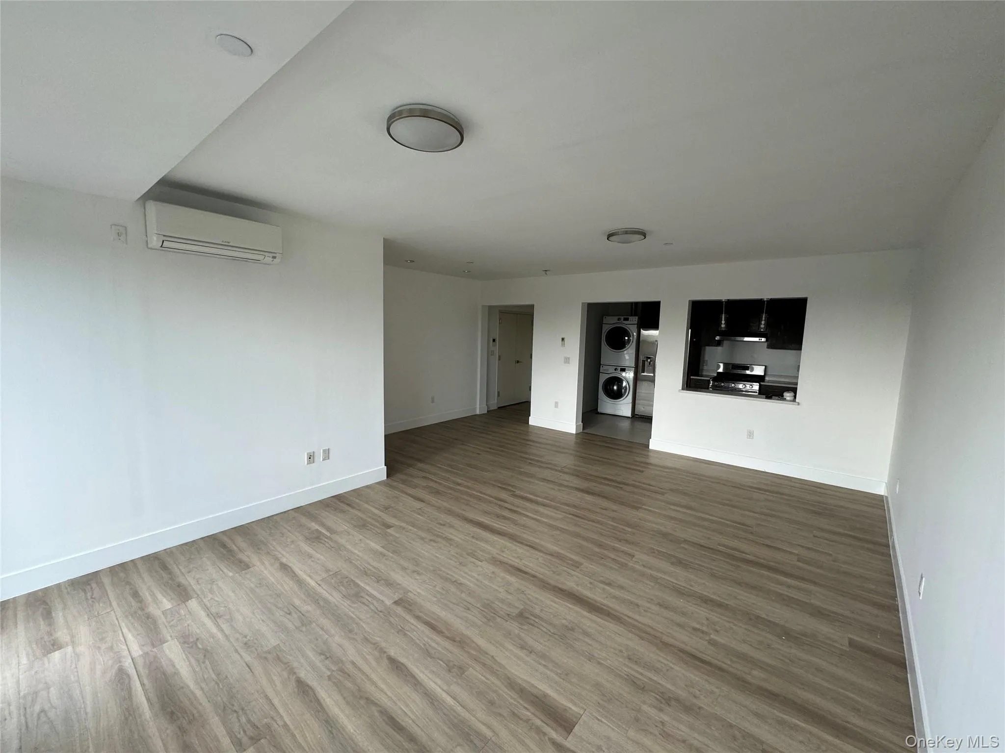 Unfurnished living room featuring stacked washer / drying machine, light wood finished floors, and a wall unit AC Unfurnished living room featuring stacked washer / drying machine, light wood finished floors, and a wall unit AC