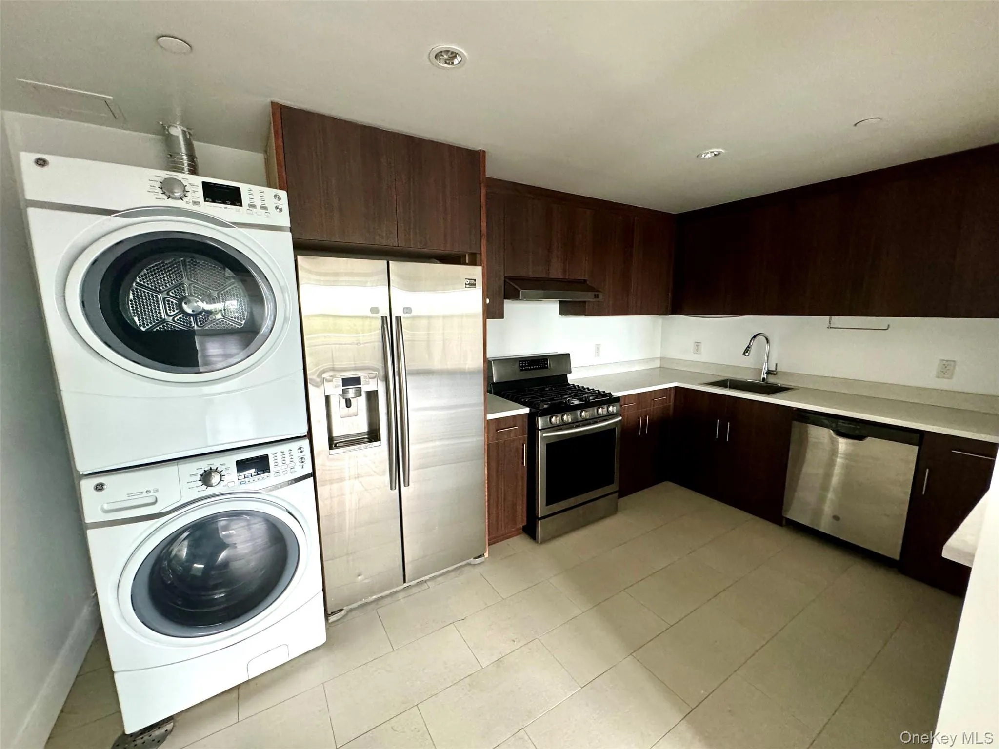 Kitchen with dark brown cabinets, stainless steel appliances, modern cabinets, stacked washing machine and dryer, and under cabinet range hood Kitchen with dark brown cabinets, stainless steel appliances, modern cabinets, stacked washing machine and dryer, and under cabinet range hood