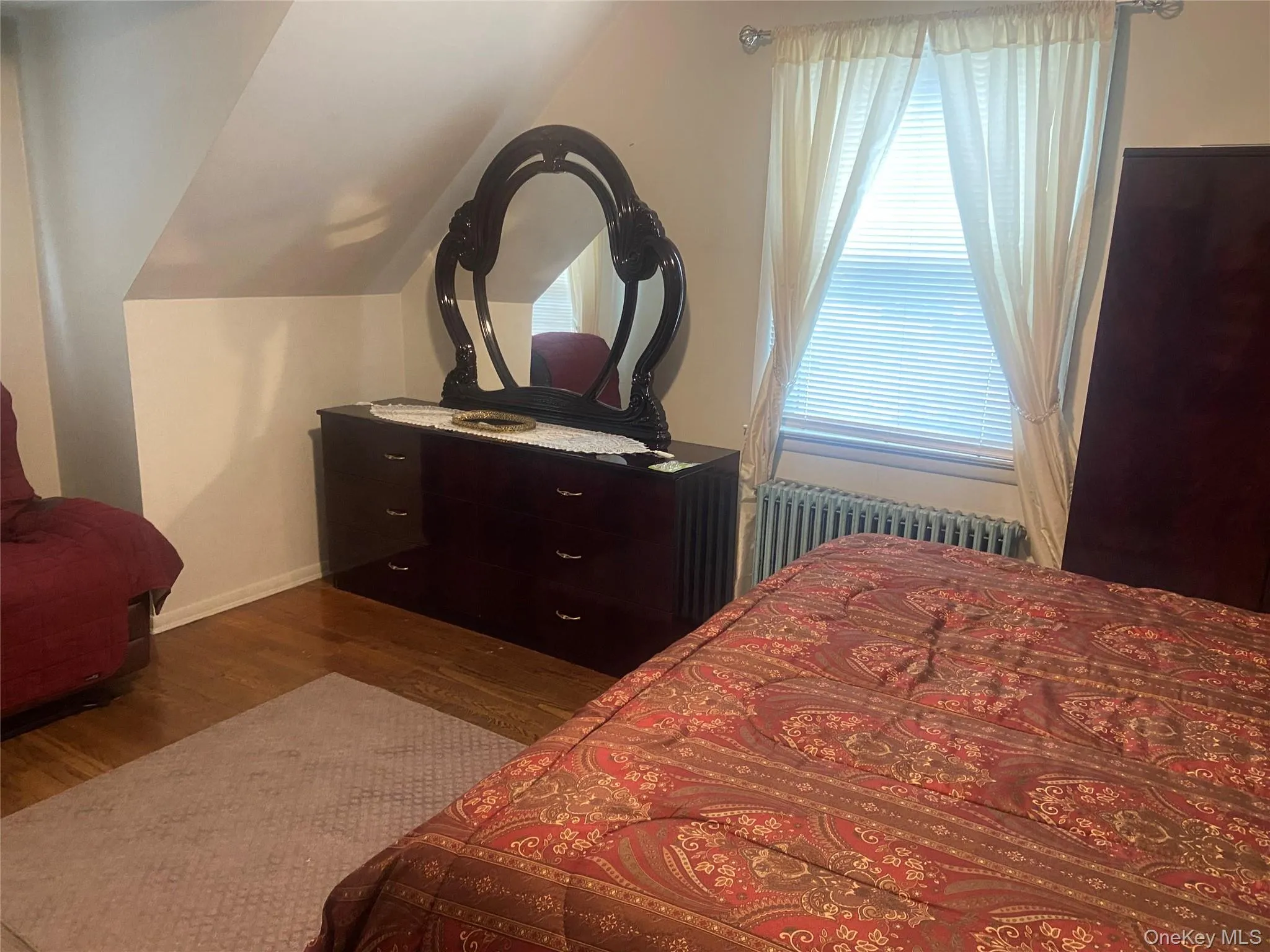Bedroom with vaulted ceiling, wood finished floors, and radiator heating unit Bedroom with vaulted ceiling, wood finished floors, and radiator heating unit