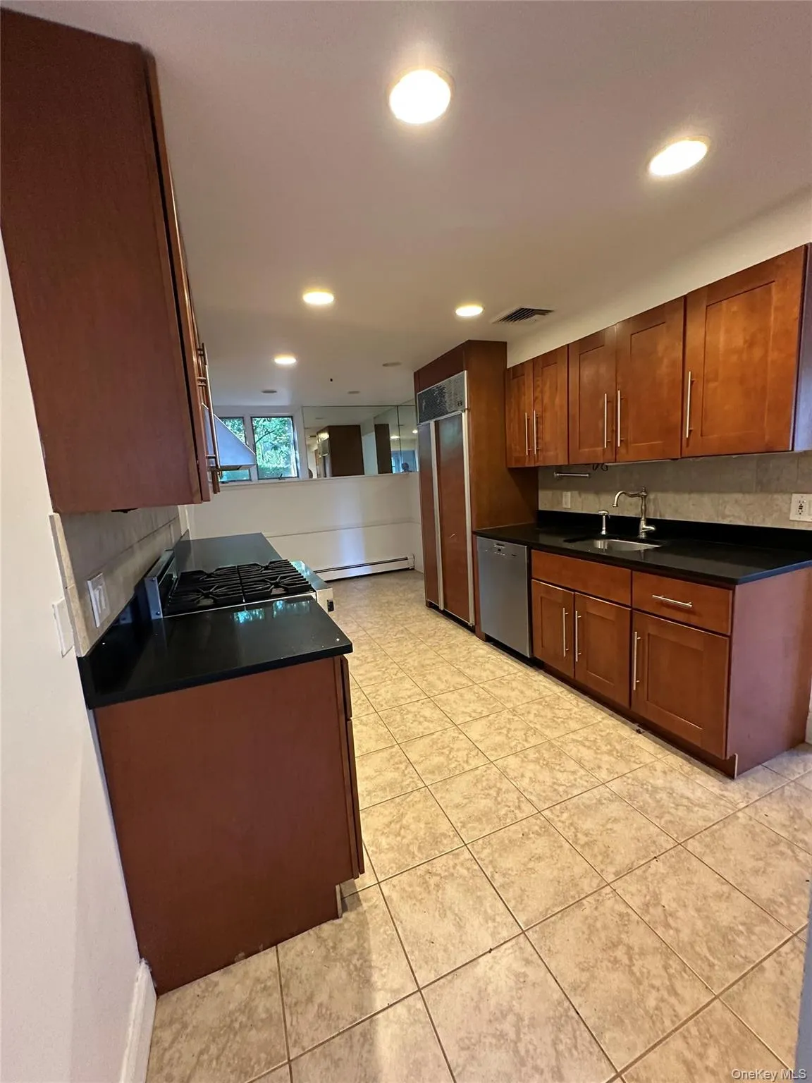 Kitchen featuring dark countertops, decorative backsplash, brown cabinets, recessed lighting, and appliances with stainless steel finishes Kitchen featuring dark countertops, decorative backsplash, brown cabinets, recessed lighting, and appliances with stainless steel finishes