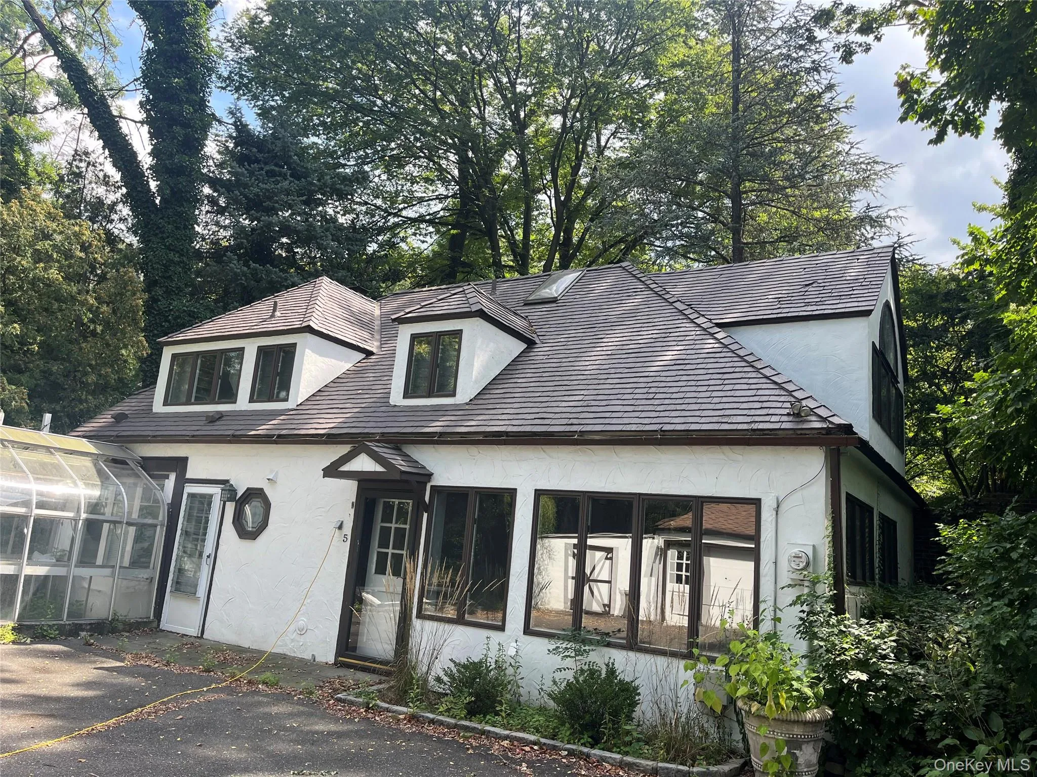 View of front of property featuring stucco siding, a sunroom, a greenhouse, and view of scattered trees View of front of property featuring stucco siding, a sunroom, a greenhouse, and view of scattered trees