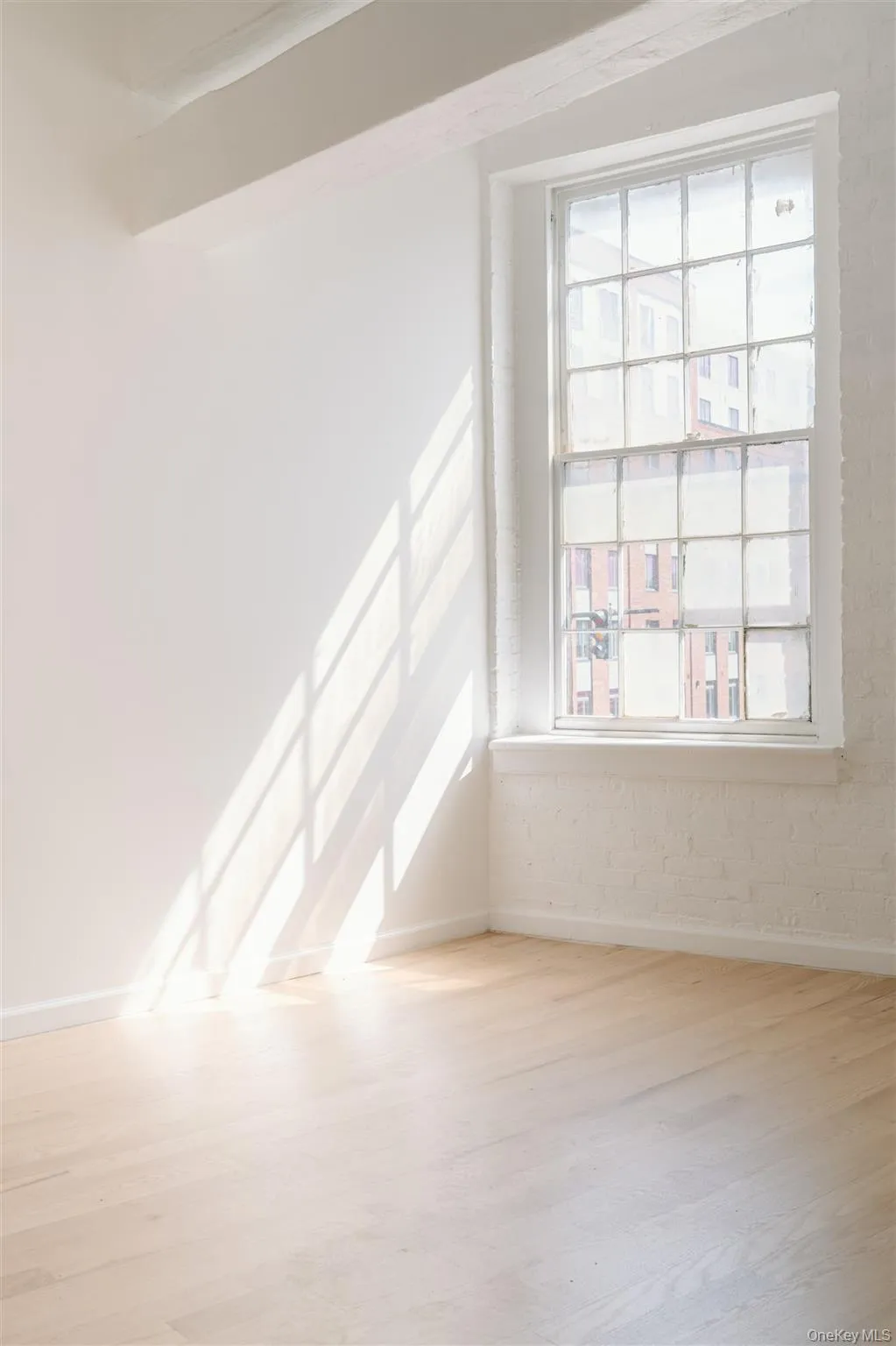 Empty room with light wood-style floors, healthy amount of natural light, and brick wall Empty room with light wood-style floors, healthy amount of natural light, and brick wall