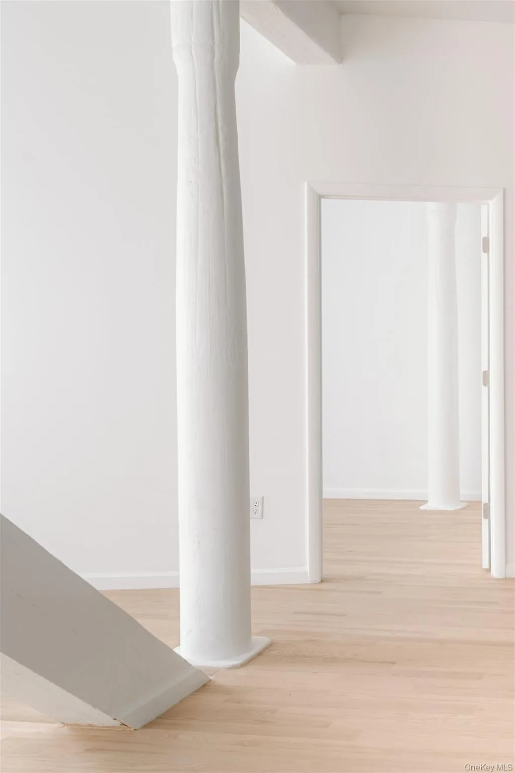 Hall featuring decorative columns and light wood-style flooring Hall featuring decorative columns and light wood-style flooring