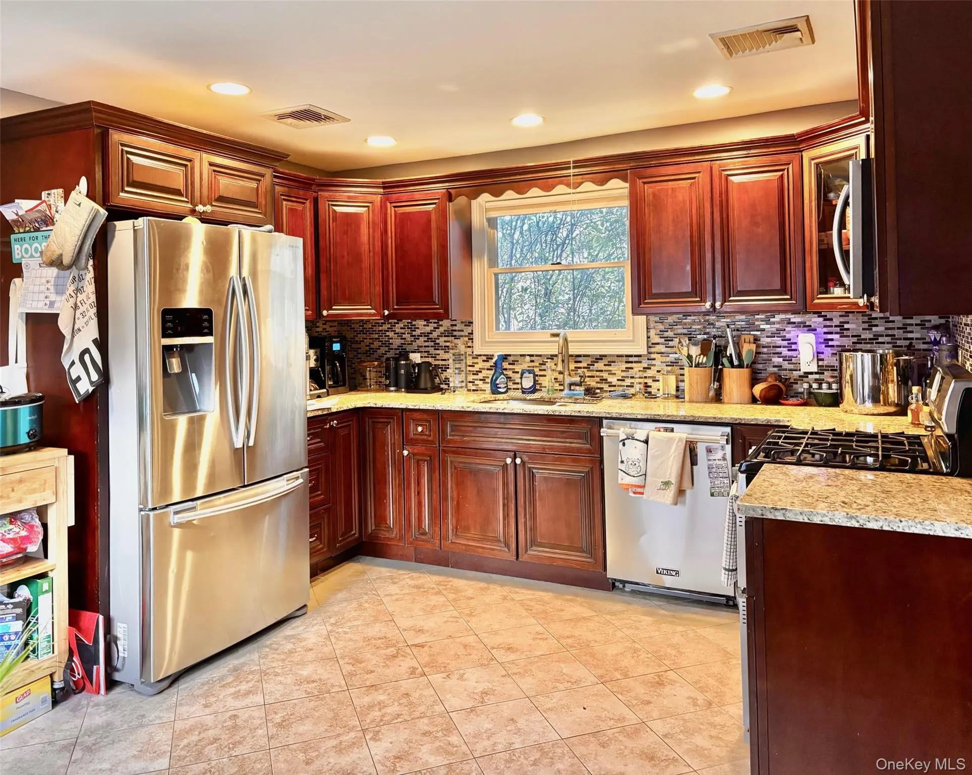 Kitchen with appliances with stainless steel finishes, recessed lighting, dark brown cabinets, light stone counters, and glass insert cabinets Kitchen with appliances with stainless steel finishes, recessed lighting, dark brown cabinets, light stone counters, and glass insert cabinets