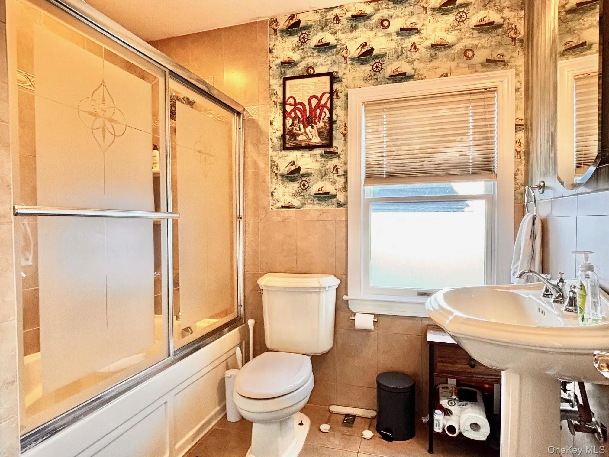 Full bath featuring shower / bath combination with glass door, tile patterned flooring, tile walls, and wainscoting Full bath featuring shower / bath combination with glass door, tile patterned flooring, tile walls, and wainscoting