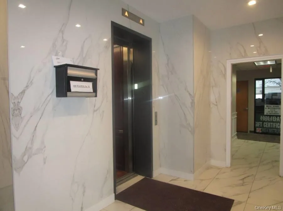 Hallway with elevator, stone wall, recessed lighting, and light marble finish flooring Hallway with elevator, stone wall, recessed lighting, and light marble finish flooring
