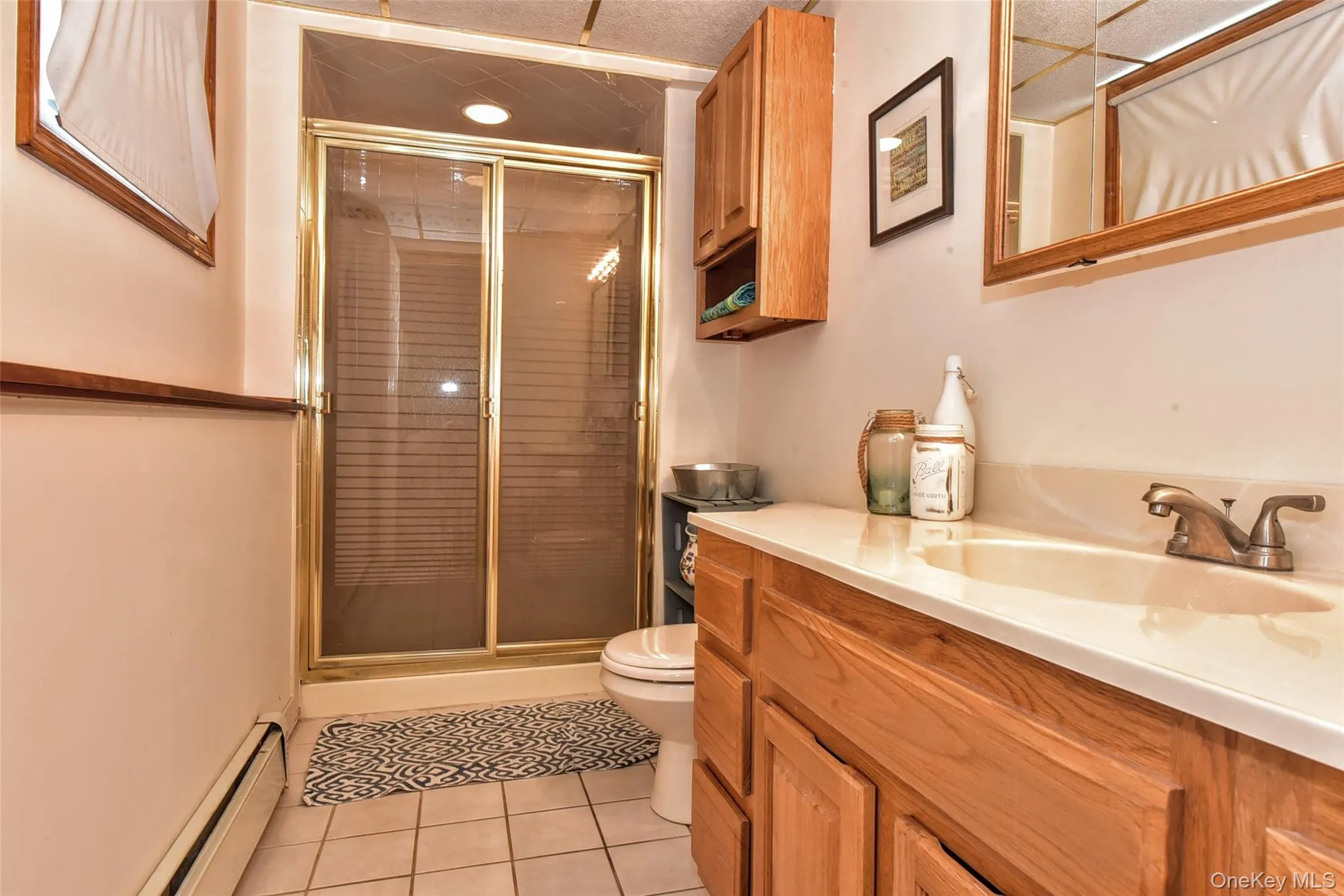 This 2nd bathroom is located on the lower level includes a shower with privacy sliding glass doors, a vanity with wood-finish cabinetry, a single basin sink, and a light-toned countertop This 2nd bathroom is located on the lower level includes a shower with privacy sliding glass doors, a vanity with wood-finish cabinetry, a single basin sink, and a light-toned countertop