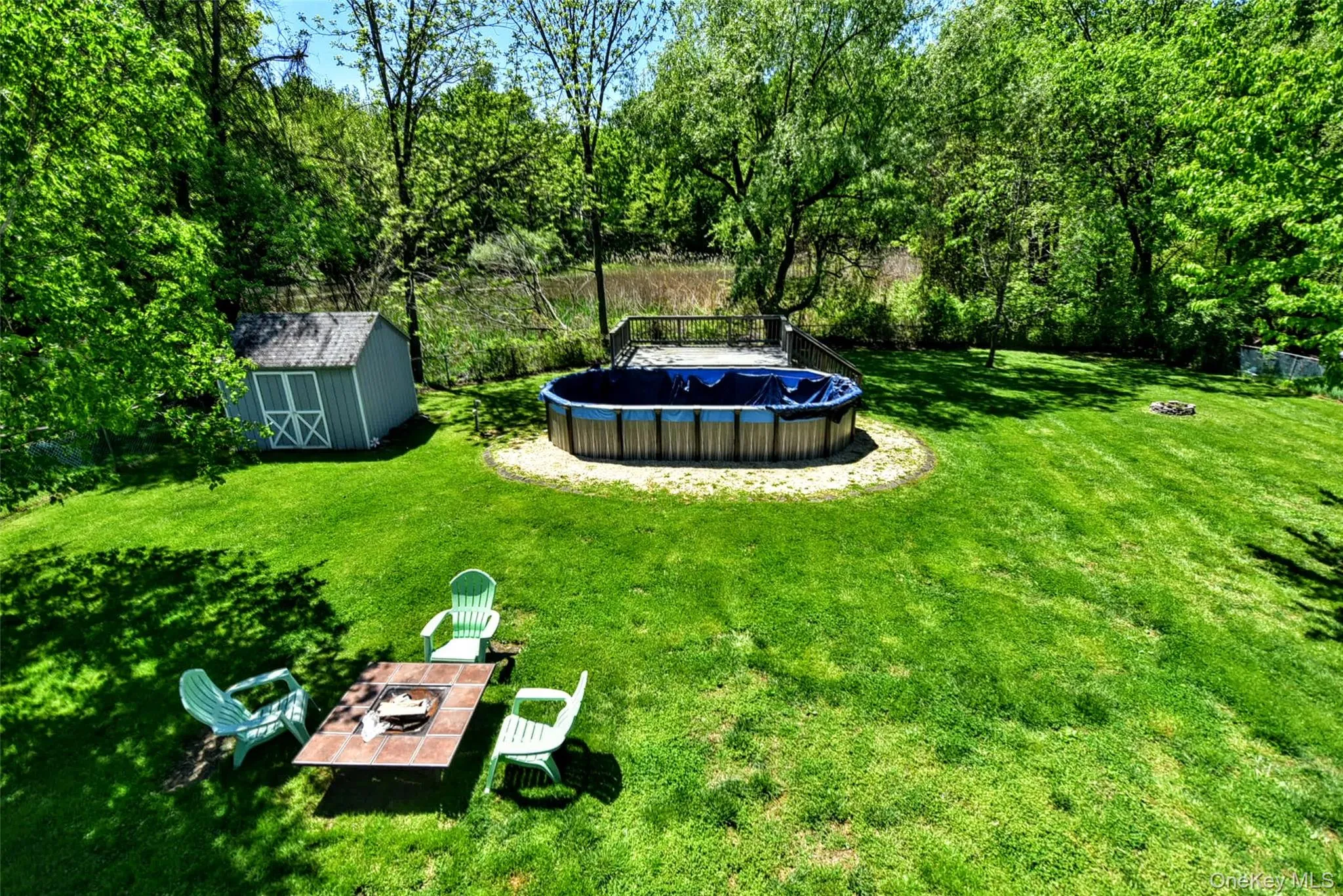 Expansive green yard with an above-ground pool, a dedicated fire pit area, and a storage shed enclosed by a chain link fence Expansive green yard with an above-ground pool, a dedicated fire pit area, and a storage shed enclosed by a chain link fence