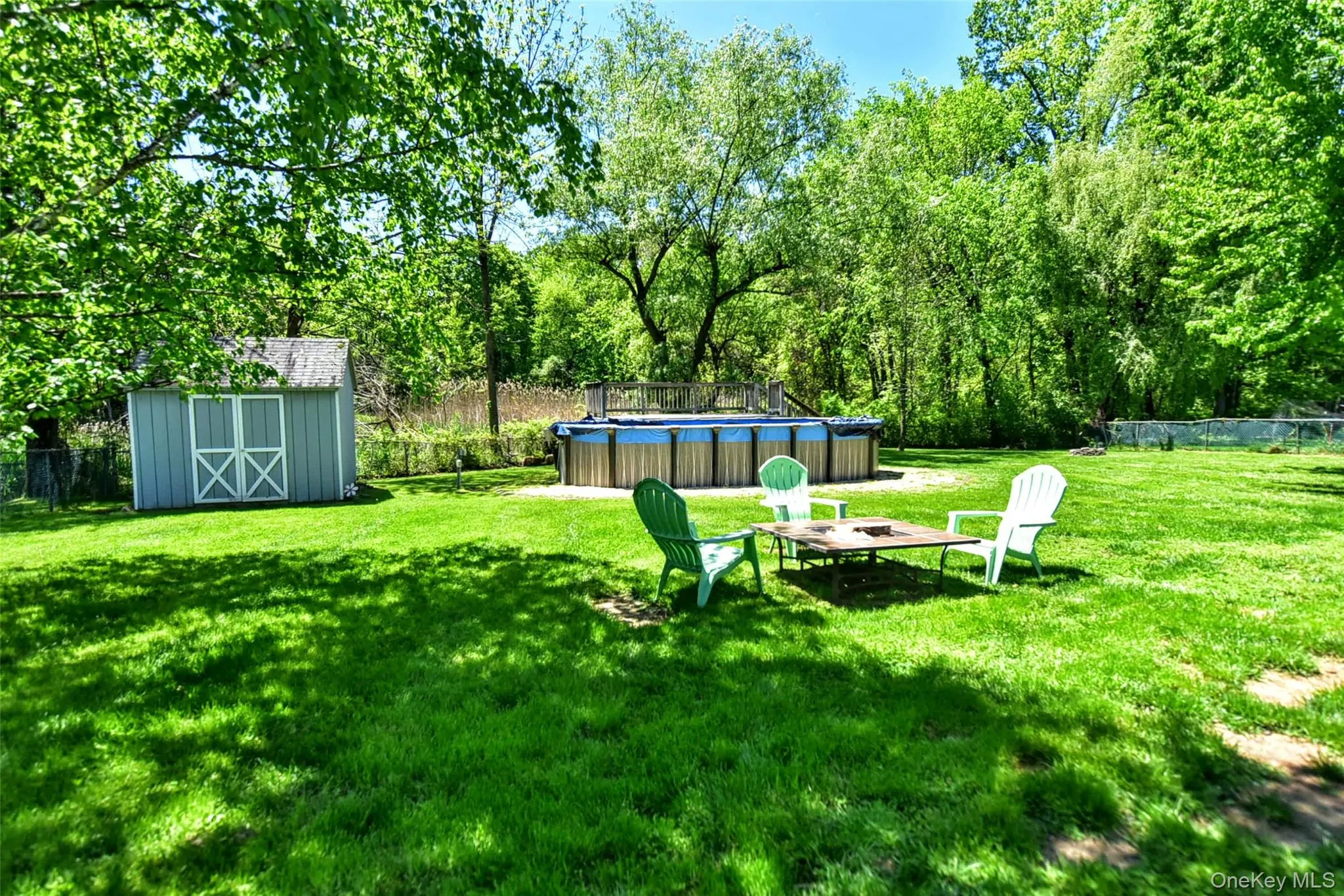Expansive rear yard featuring a large above-ground pool, a light blue storage shed with white barn doors, and mature perimeter trees providing shade Expansive rear yard featuring a large above-ground pool, a light blue storage shed with white barn doors, and mature perimeter trees providing shade