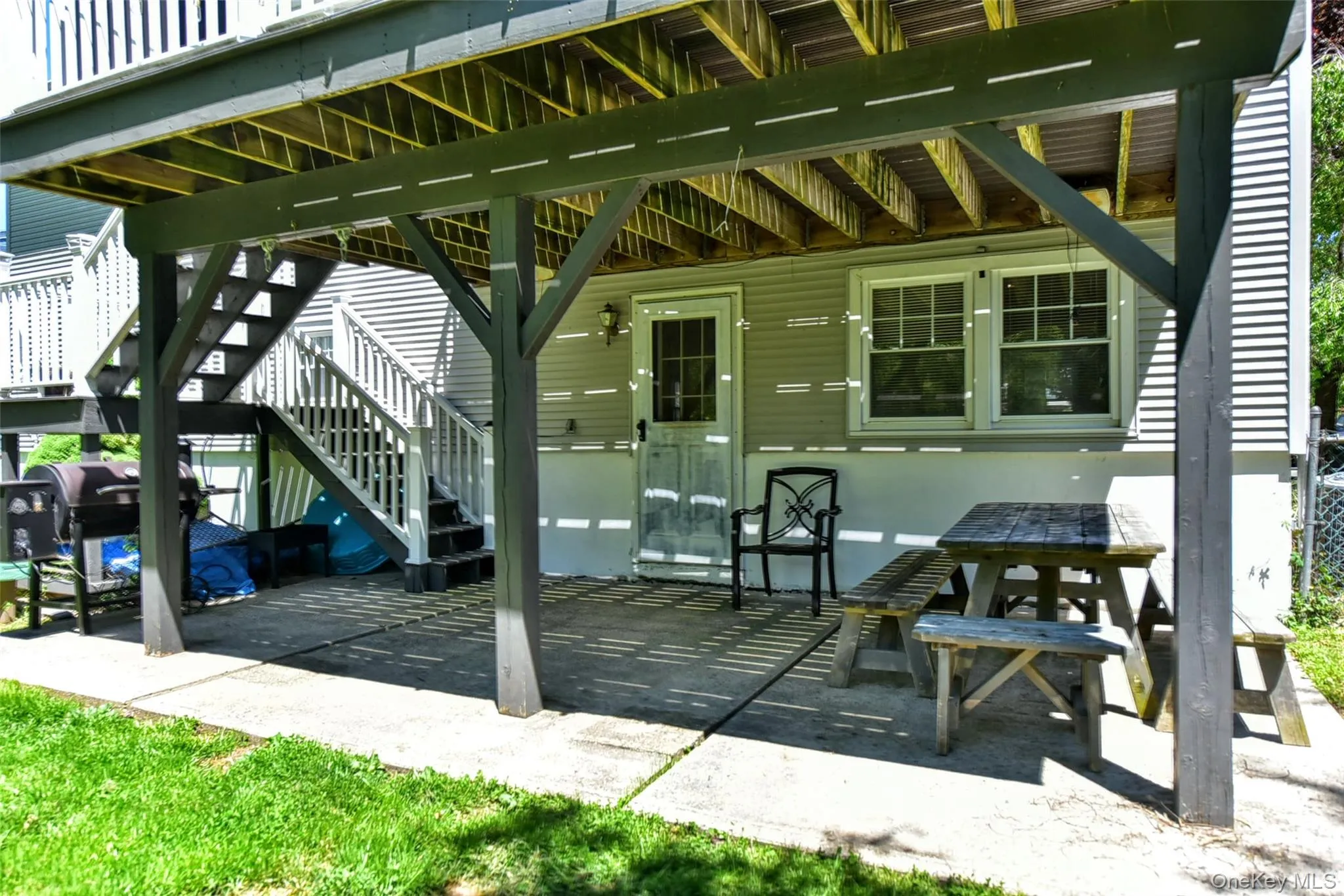 Covered patio area under a raised deck, featuring a concrete surface, exterior siding, and a door leading into to the recreation room Covered patio area under a raised deck, featuring a concrete surface, exterior siding, and a door leading into to the recreation room
