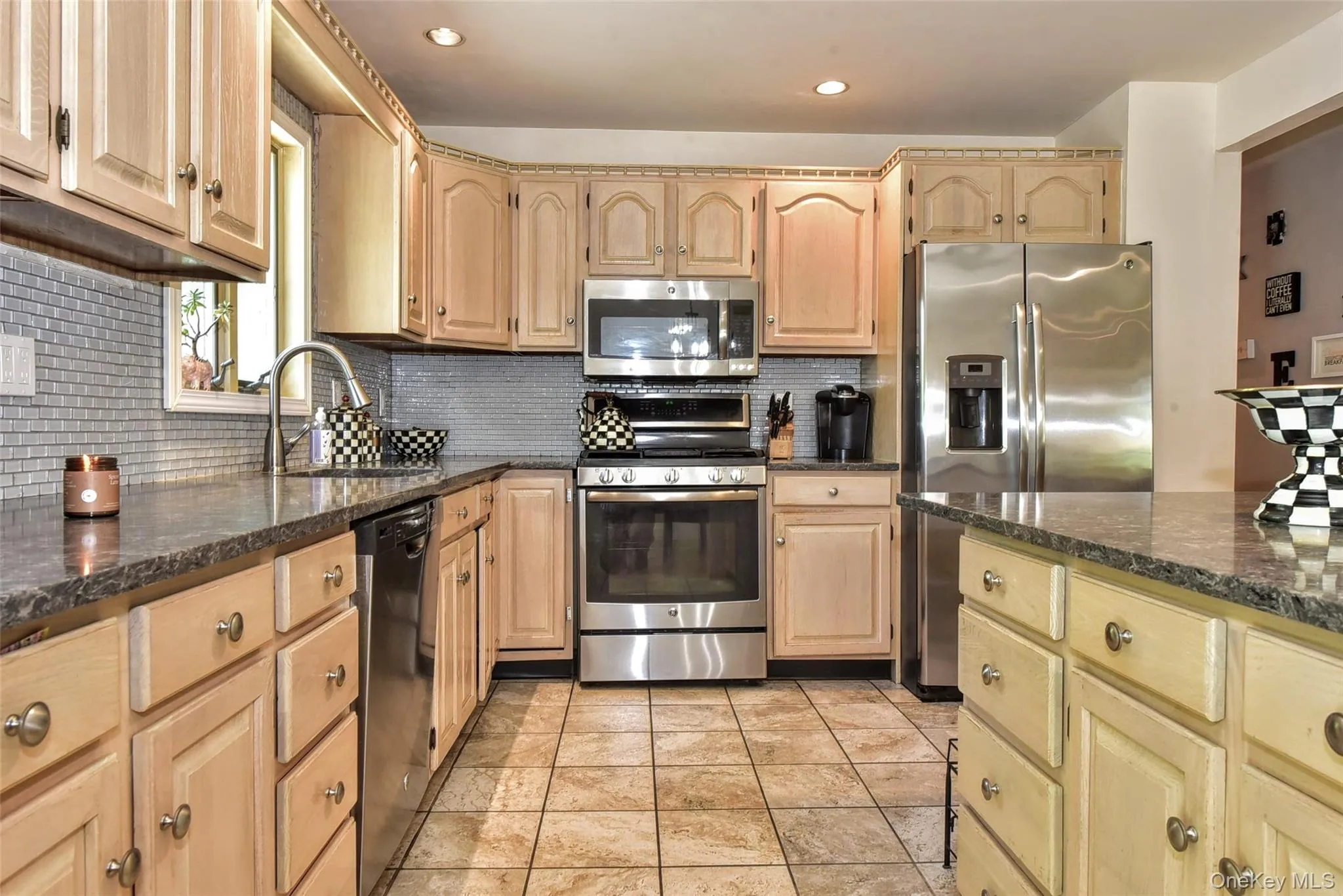 Kitchen featuring light wood cabinetry, stone-finish countertops, stainless steel appliances and a tiled backsplash Kitchen featuring light wood cabinetry, stone-finish countertops, stainless steel appliances and a tiled backsplash