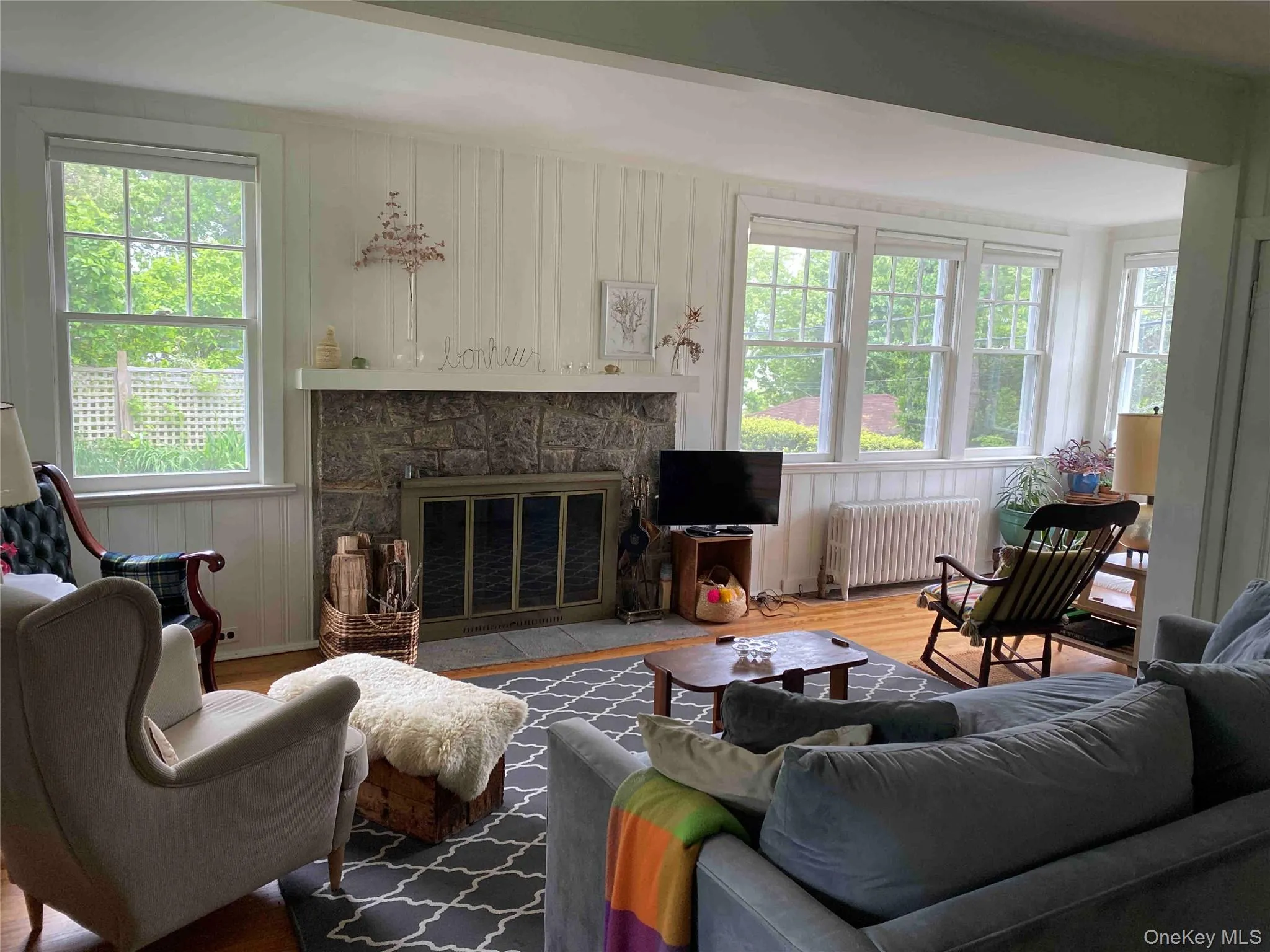 Living room with wood finished floors, a stone fireplace, radiator heating unit, and wood walls Living room with wood finished floors, a stone fireplace, radiator heating unit, and wood walls