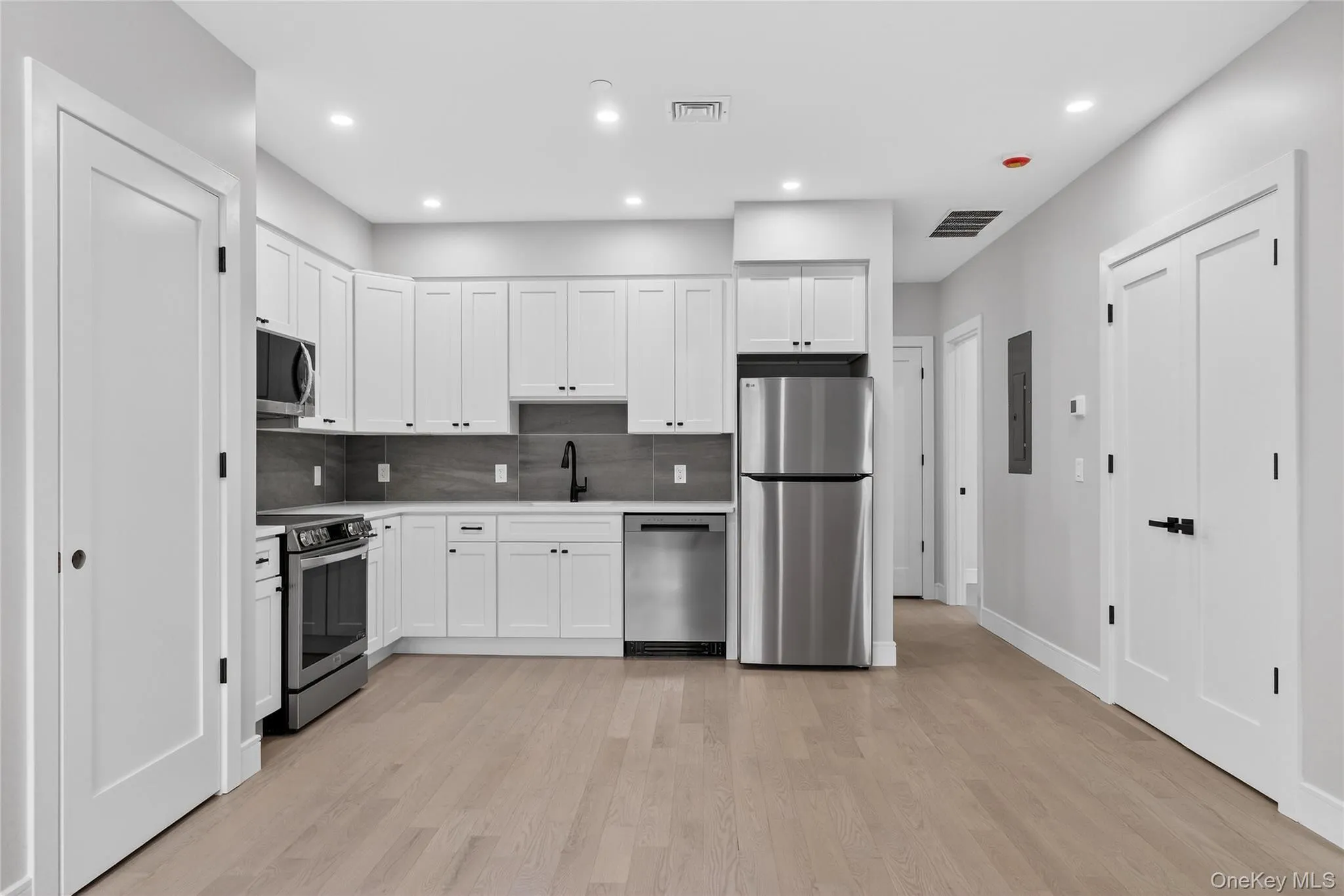 Kitchen featuring white cabinetry, stainless steel appliances, recessed lighting, decorative backsplash, and light wood-style flooring Kitchen featuring white cabinetry, stainless steel appliances, recessed lighting, decorative backsplash, and light wood-style flooring