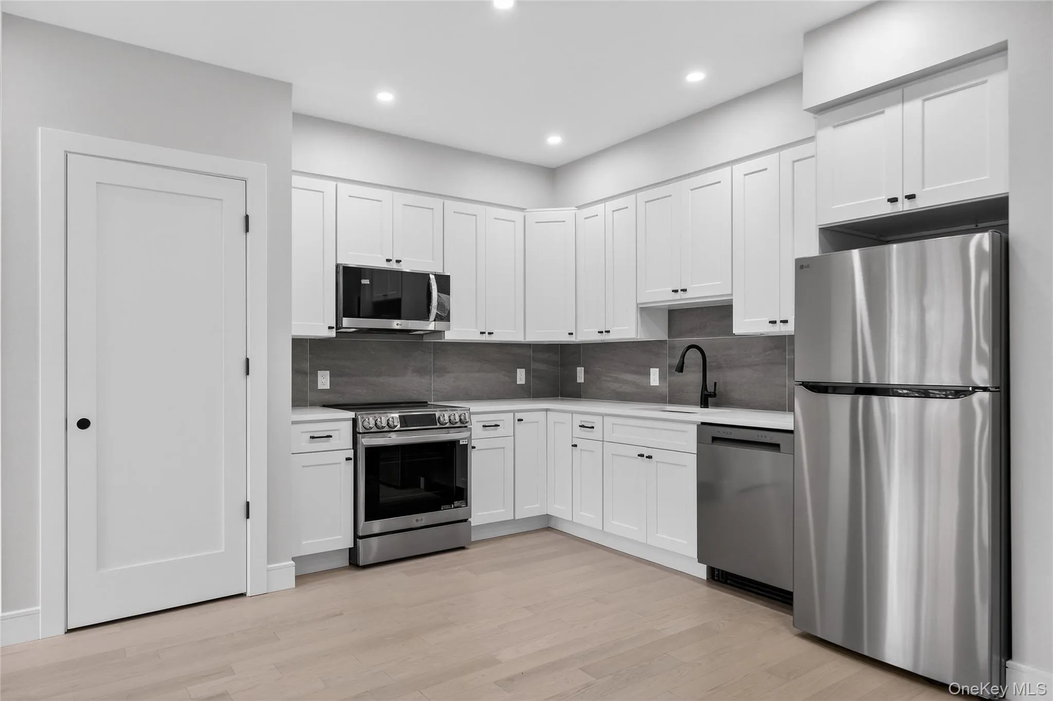 Kitchen featuring appliances with stainless steel finishes, white cabinetry, tasteful backsplash, light wood-type flooring, and recessed lighting Kitchen featuring appliances with stainless steel finishes, white cabinetry, tasteful backsplash, light wood-type flooring, and recessed lighting