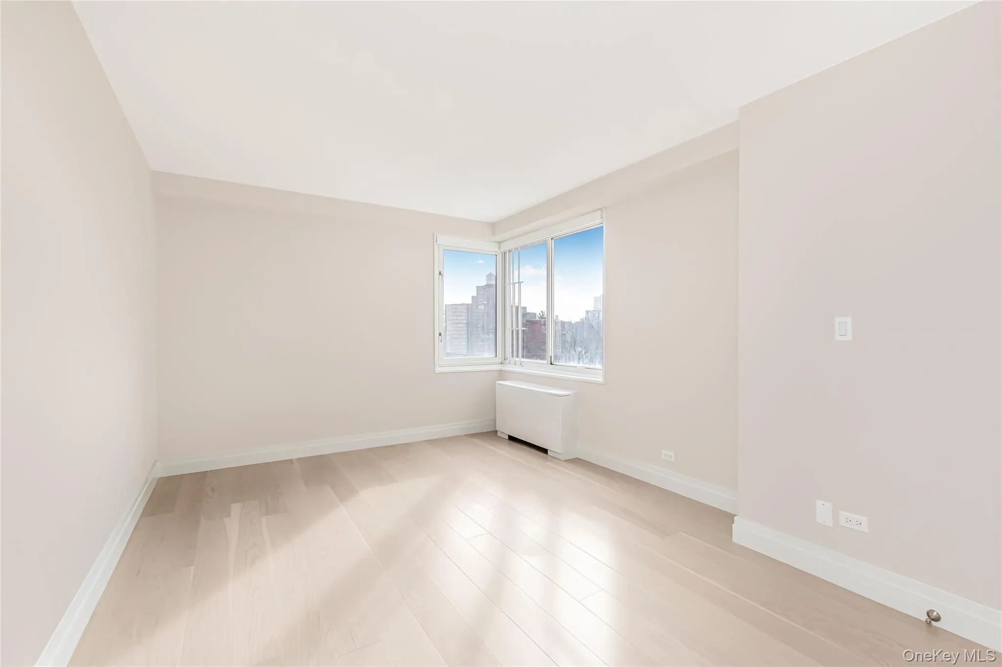 Unfurnished room with radiator heating unit, light wood-style flooring, and a view of city Unfurnished room with radiator heating unit, light wood-style flooring, and a view of city