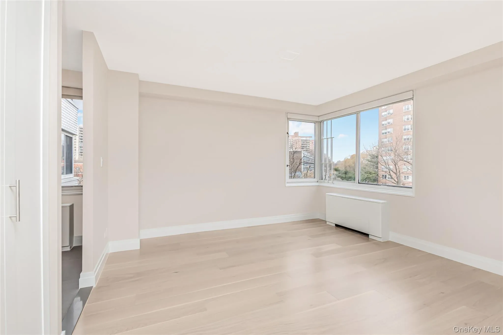 Unfurnished room with radiator, plenty of natural light, light wood-style flooring, and a city view Unfurnished room with radiator, plenty of natural light, light wood-style flooring, and a city view