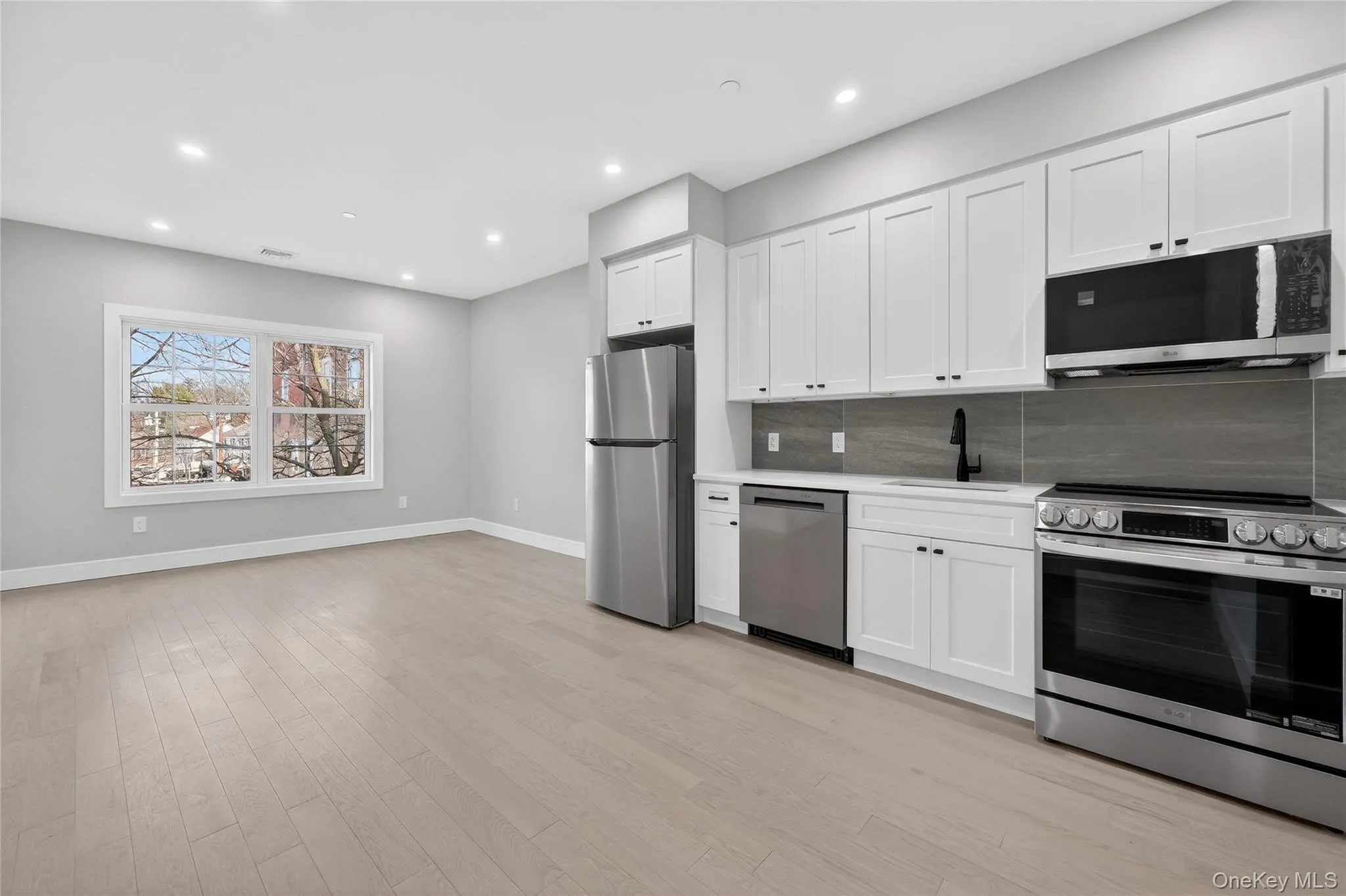Kitchen with appliances with stainless steel finishes, white cabinetry, backsplash, recessed lighting, and light wood-type flooring Kitchen with appliances with stainless steel finishes, white cabinetry, backsplash, recessed lighting, and light wood-type flooring