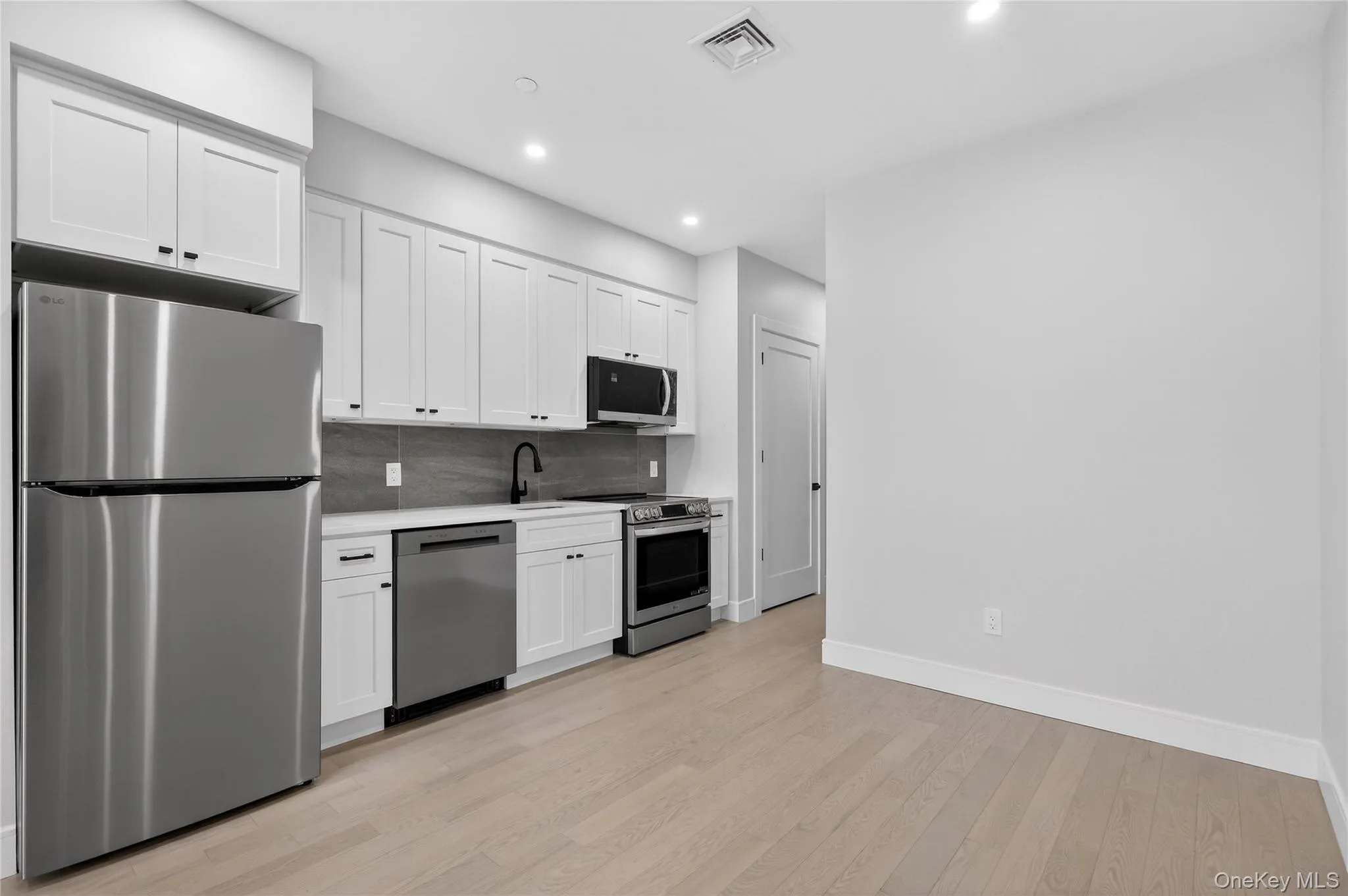 Kitchen with stainless steel appliances, white cabinetry, light countertops, tasteful backsplash, and light wood-style flooring Kitchen with stainless steel appliances, white cabinetry, light countertops, tasteful backsplash, and light wood-style flooring
