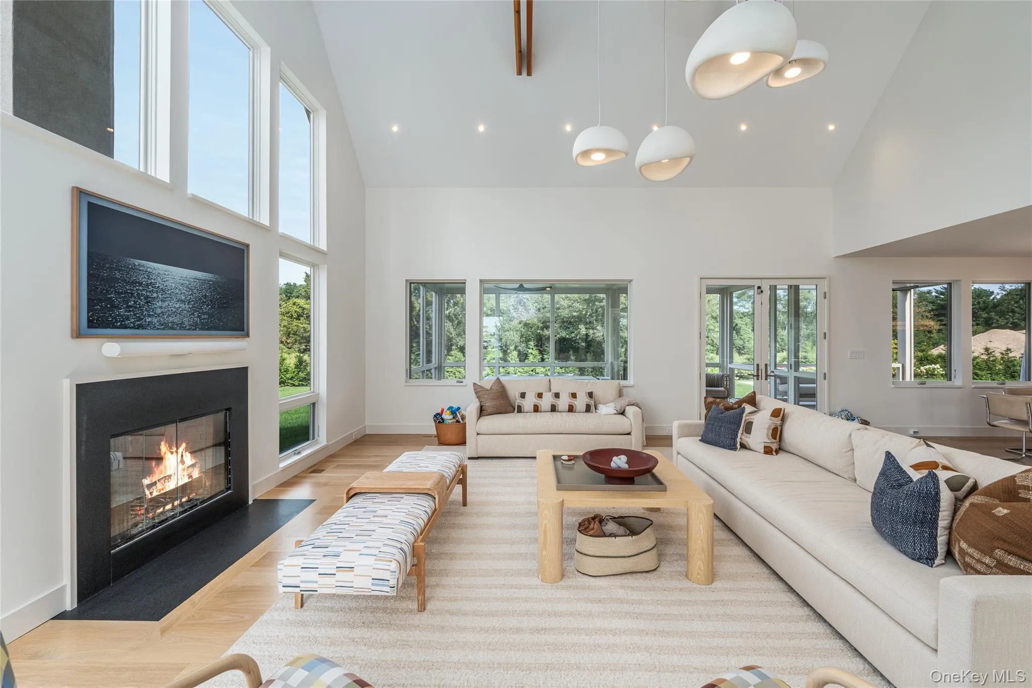 Living room featuring wood finished floors, high vaulted ceiling, a glass covered fireplace, french doors, and recessed lighting Living room featuring wood finished floors, high vaulted ceiling, a glass covered fireplace, french doors, and recessed lighting