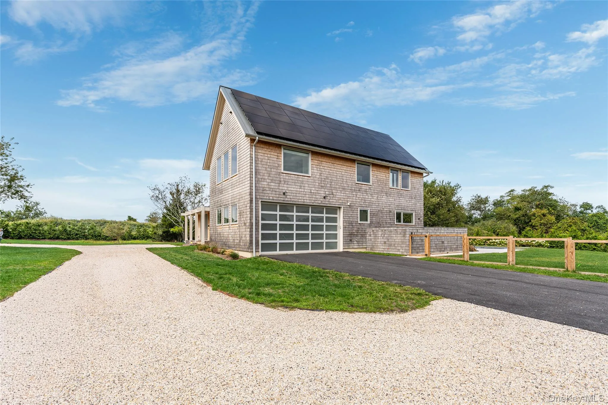 View of side of property with driveway, roof mounted solar panels, a garage, and a shingled roof View of side of property with driveway, roof mounted solar panels, a garage, and a shingled roof