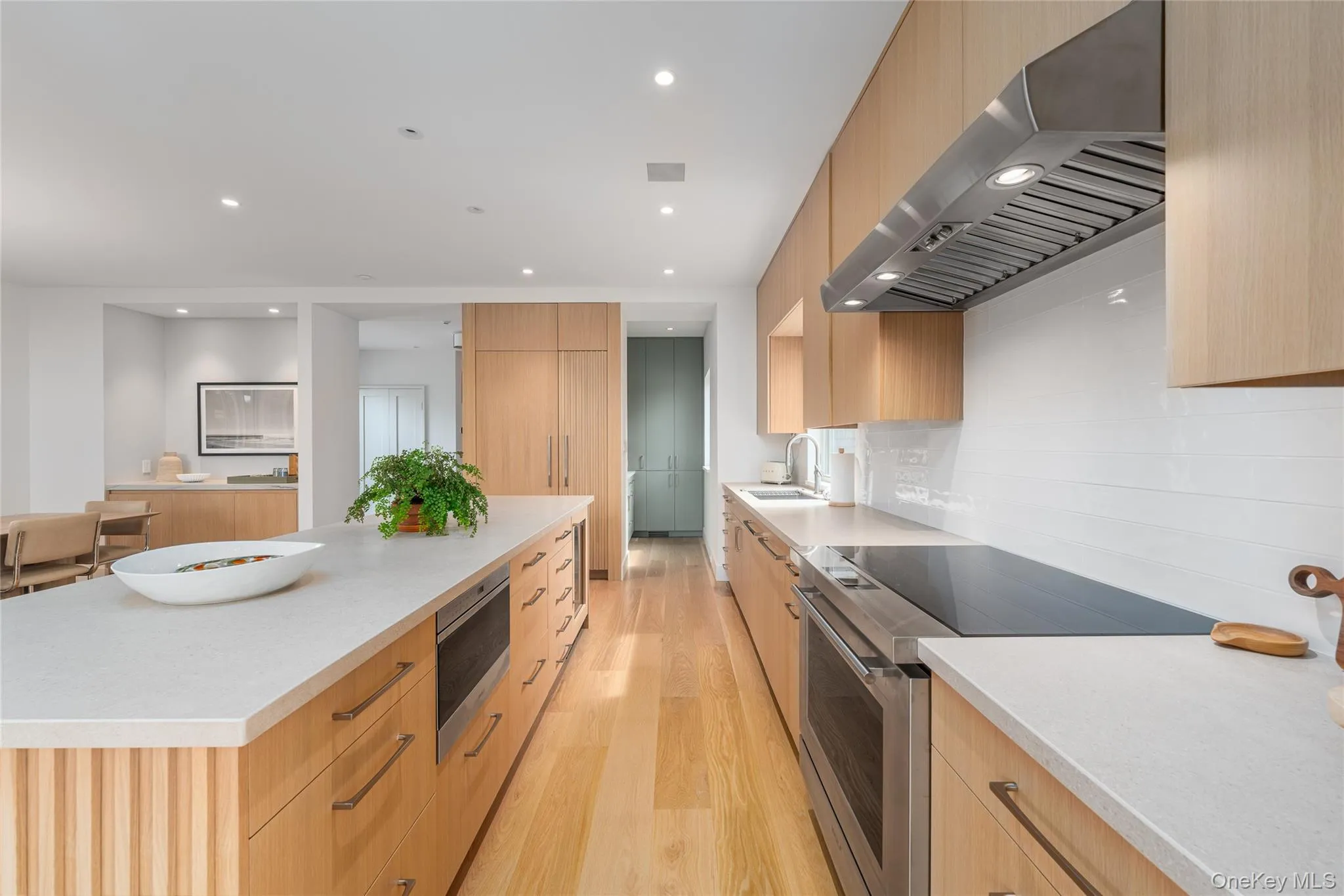 Kitchen with under cabinet range hood, modern cabinets, stainless steel appliances, light wood-style flooring, and light stone countertops Kitchen with under cabinet range hood, modern cabinets, stainless steel appliances, light wood-style flooring, and light stone countertops