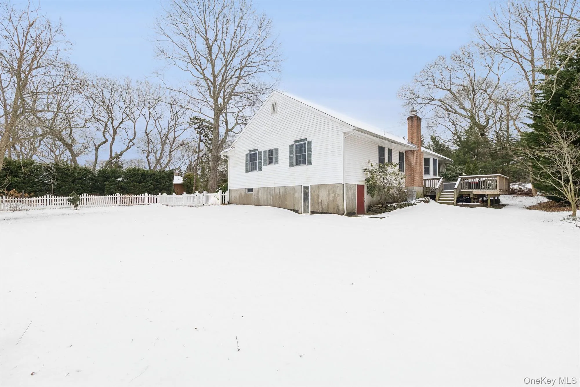 View of snowy exterior with a chimney and a wooden deck View of snowy exterior with a chimney and a wooden deck