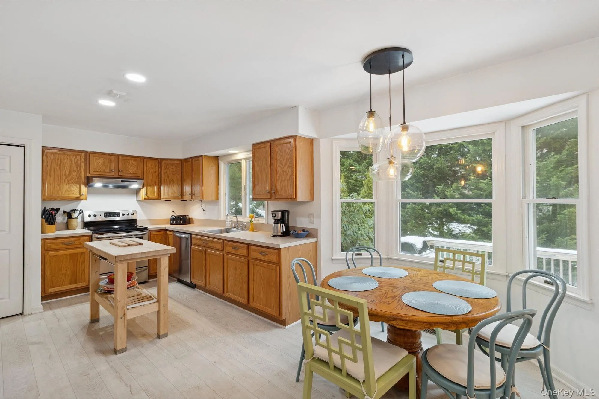 Kitchen featuring light countertops, stainless steel appliances, pendant lighting, light wood-style flooring, and brown cabinetry Kitchen featuring light countertops, stainless steel appliances, pendant lighting, light wood-style flooring, and brown cabinetry