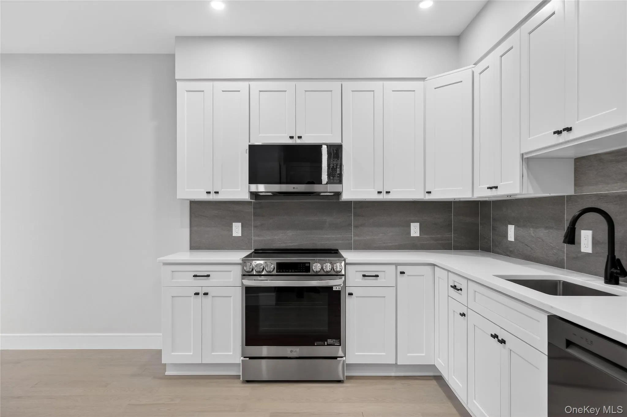 Kitchen with appliances with stainless steel finishes, white cabinetry, light wood finished floors, backsplash, and recessed lighting Kitchen with appliances with stainless steel finishes, white cabinetry, light wood finished floors, backsplash, and recessed lighting