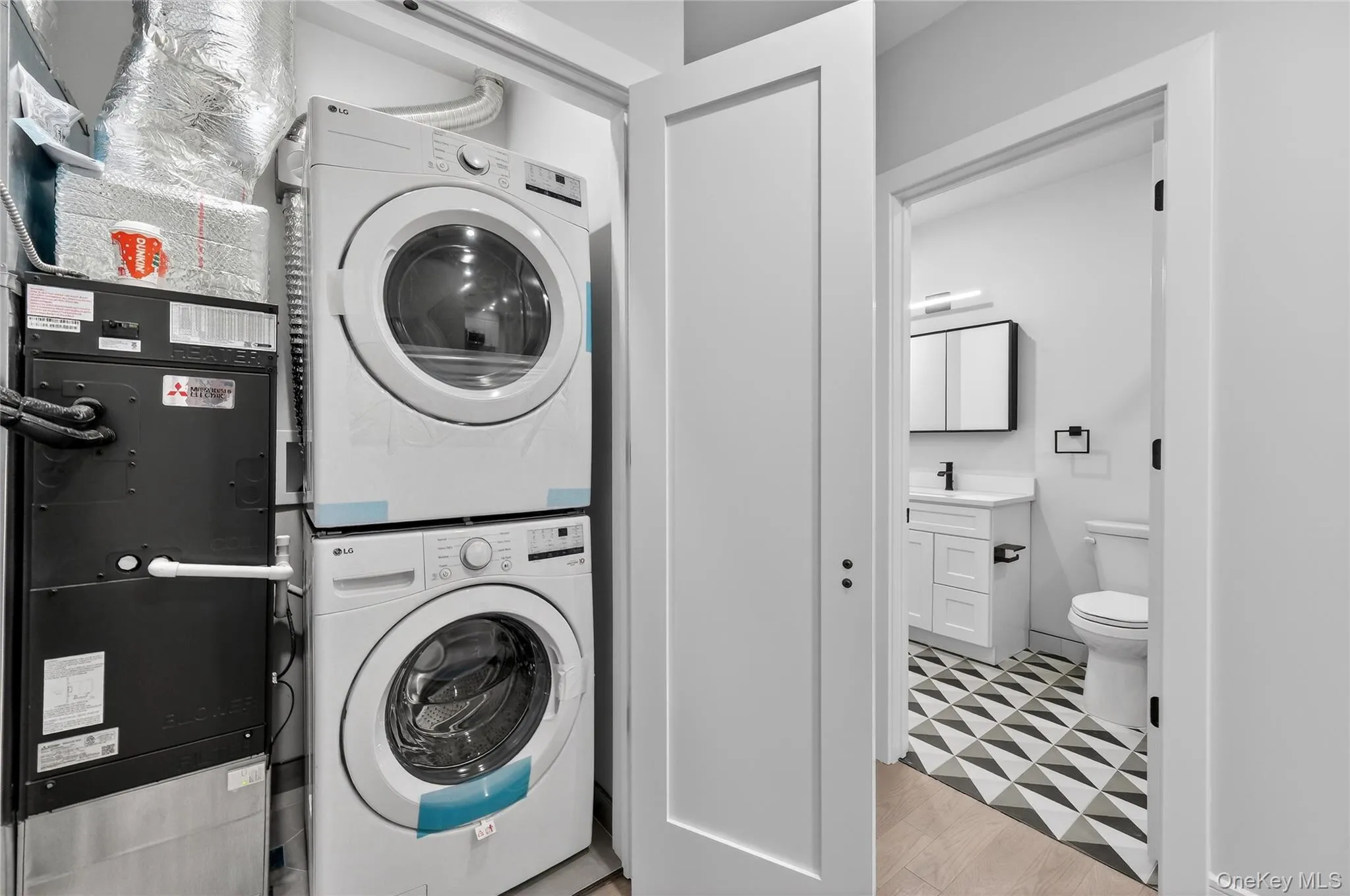 Laundry room with stacked washer / dryer, light wood finished floors, and heating unit Laundry room with stacked washer / dryer, light wood finished floors, and heating unit