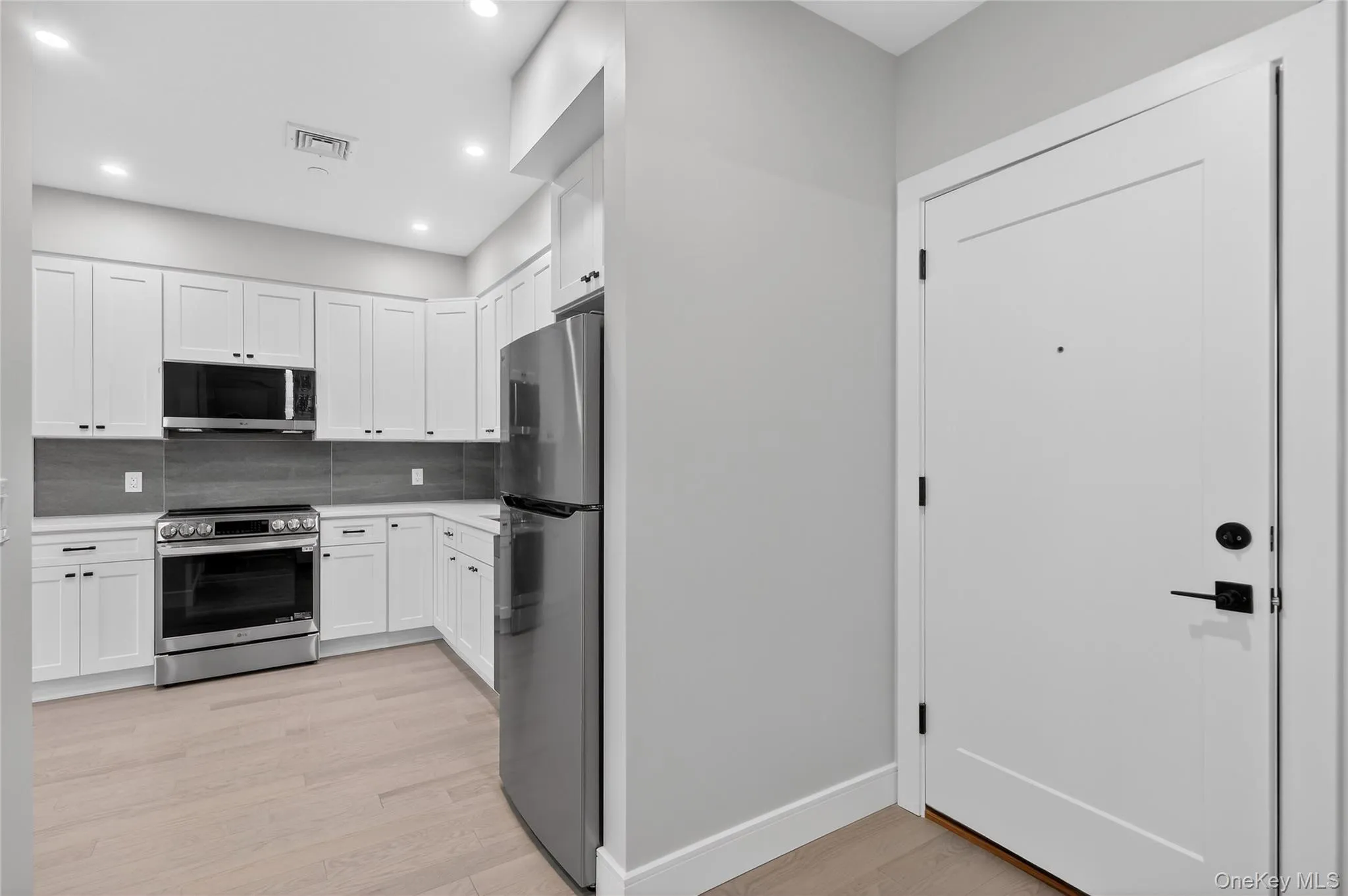 Kitchen with appliances with stainless steel finishes, white cabinets, light wood-style floors, backsplash, and recessed lighting Kitchen with appliances with stainless steel finishes, white cabinets, light wood-style floors, backsplash, and recessed lighting