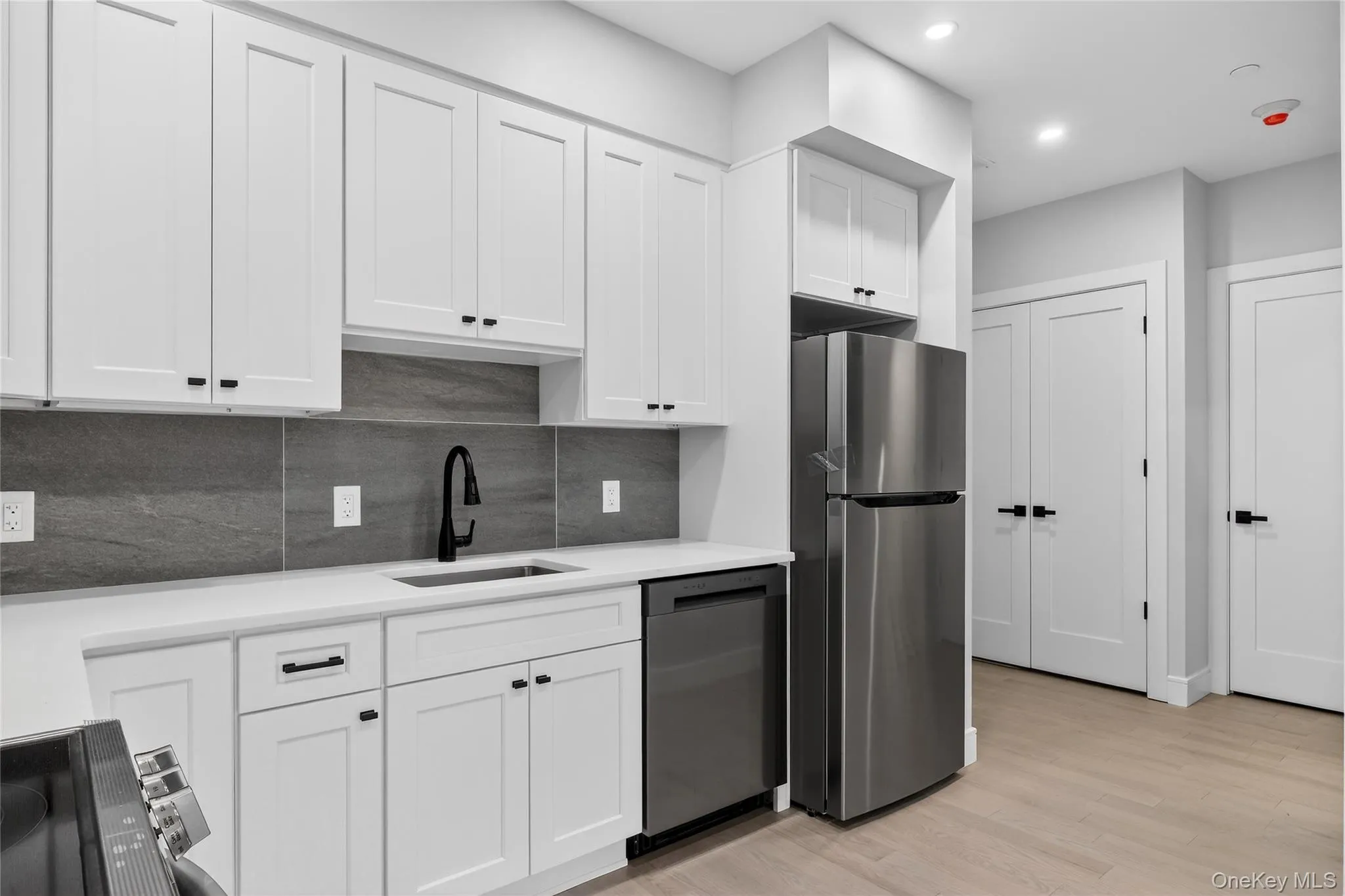Kitchen with white cabinetry, freestanding refrigerator, black electric range, tasteful backsplash, and light wood-style flooring Kitchen with white cabinetry, freestanding refrigerator, black electric range, tasteful backsplash, and light wood-style flooring