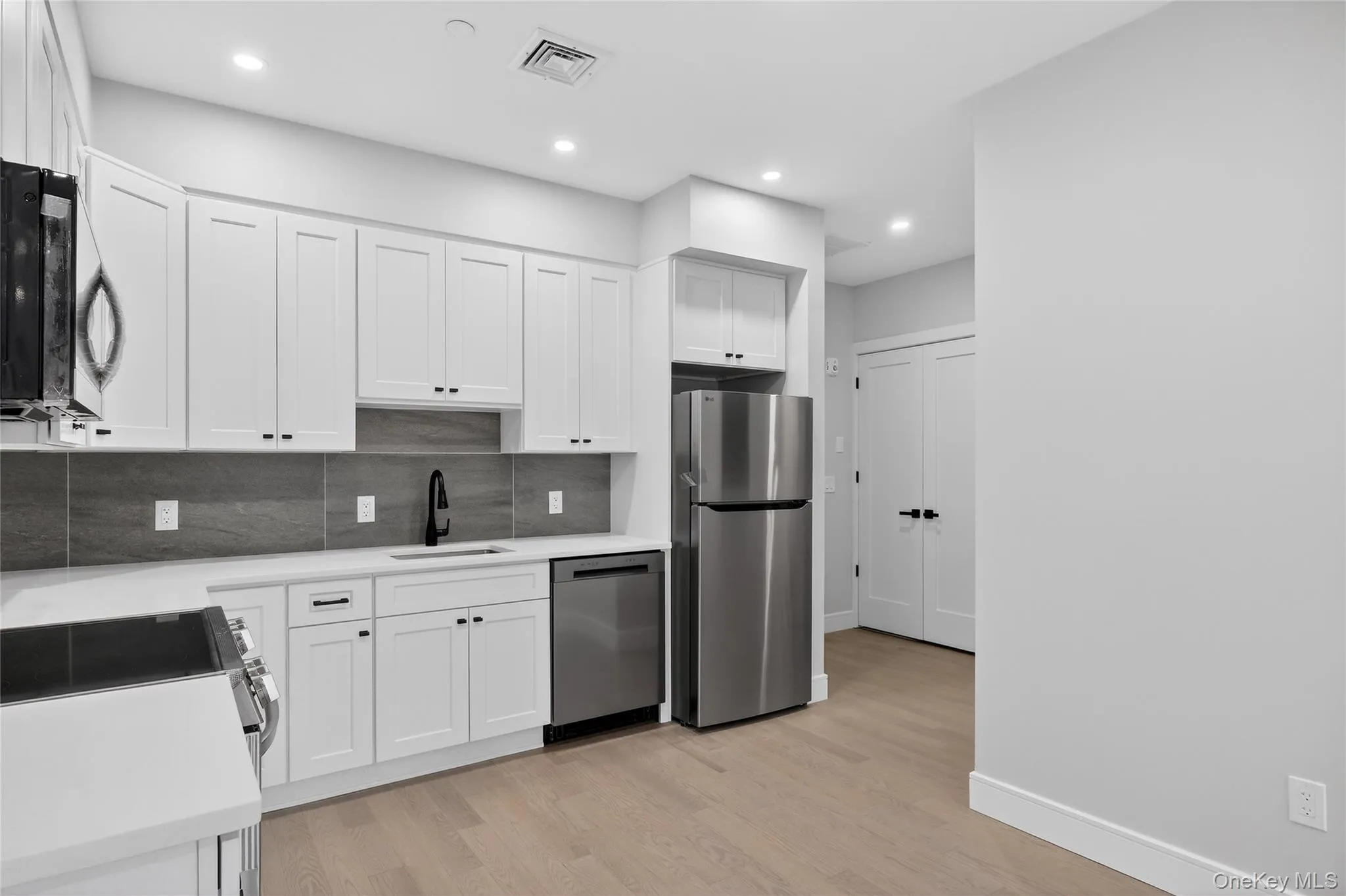 Kitchen featuring white cabinets, tasteful backsplash, appliances with stainless steel finishes, light wood-style floors, and recessed lighting Kitchen featuring white cabinets, tasteful backsplash, appliances with stainless steel finishes, light wood-style floors, and recessed lighting