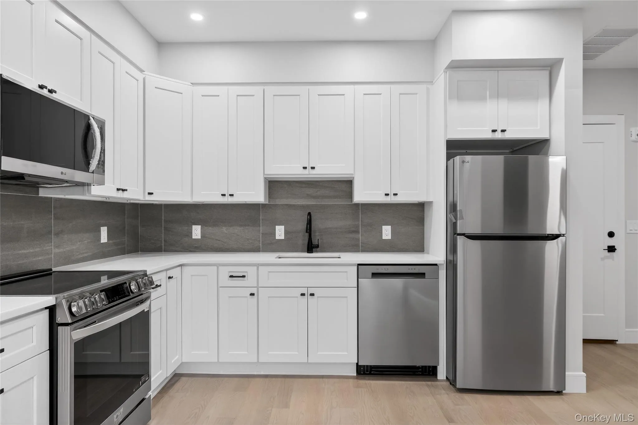 Kitchen featuring appliances with stainless steel finishes, white cabinets, light wood-type flooring, backsplash, and recessed lighting Kitchen featuring appliances with stainless steel finishes, white cabinets, light wood-type flooring, backsplash, and recessed lighting