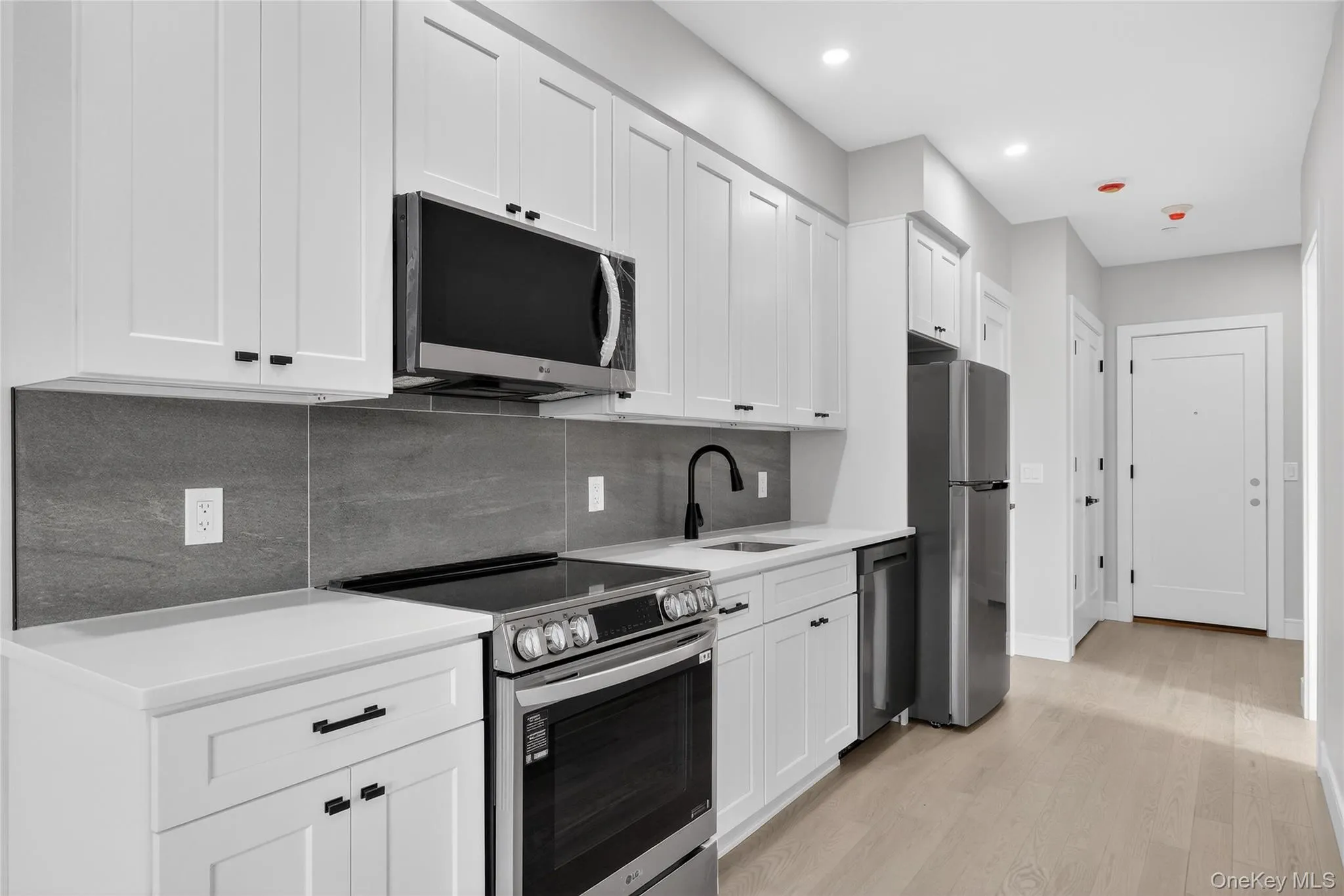 Kitchen with stainless steel appliances, white cabinetry, backsplash, light wood-style flooring, and light stone counters Kitchen with stainless steel appliances, white cabinetry, backsplash, light wood-style flooring, and light stone counters