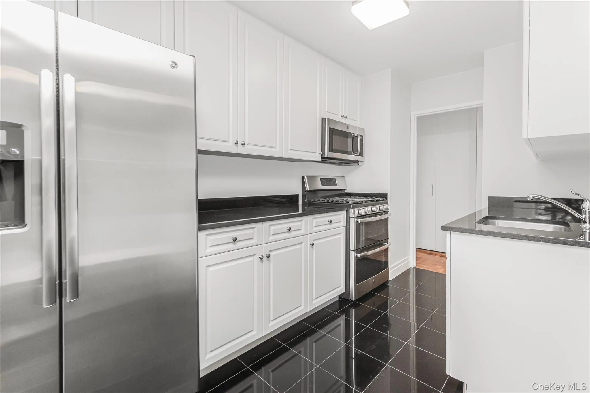 Kitchen with stainless steel appliances, white cabinetry, dark stone countertops, and granite floors Kitchen with stainless steel appliances, white cabinetry, dark stone countertops, and granite floors
