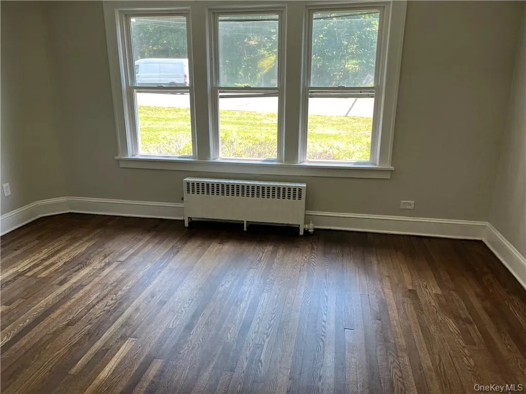 Empty room with a wealth of natural light, dark hardwood / wood-style floors, and radiator Empty room with a wealth of natural light, dark hardwood / wood-style floors, and radiator