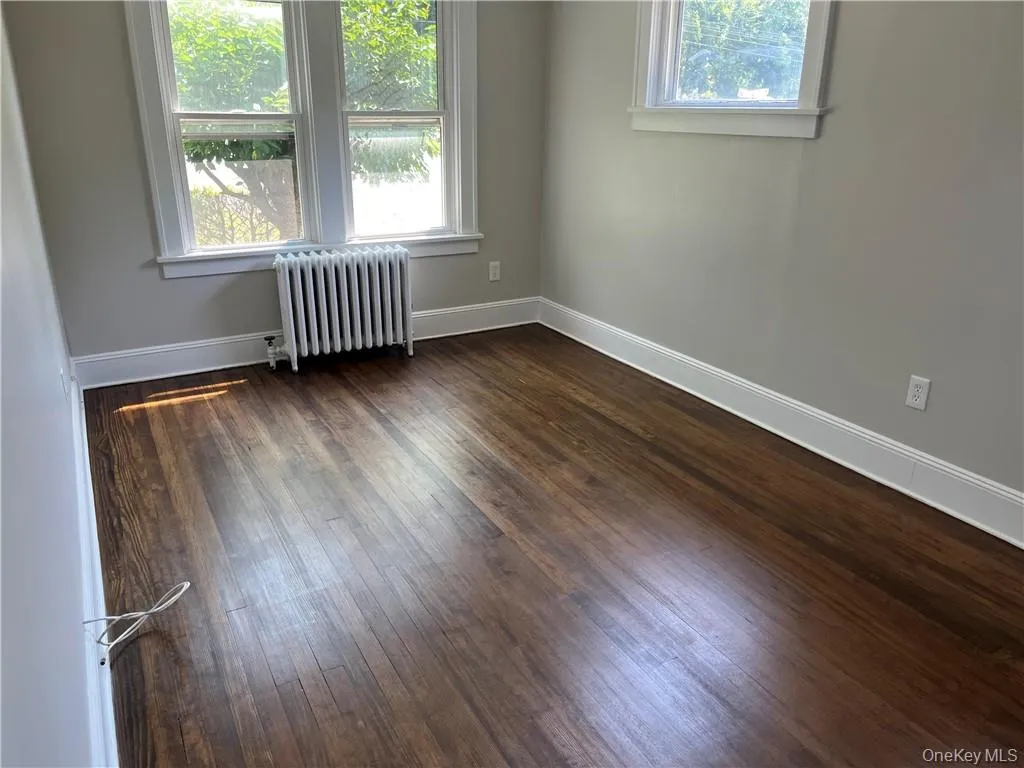Empty room with dark hardwood / wood-style flooring and radiator heating unit Empty room with dark hardwood / wood-style flooring and radiator heating unit