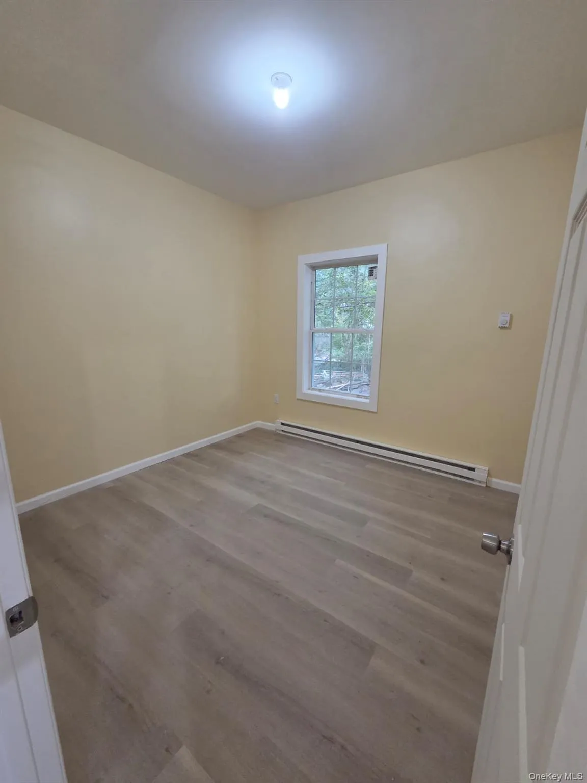 Unfurnished room with baseboard heating and light wood-style floors Unfurnished room with baseboard heating and light wood-style floors
