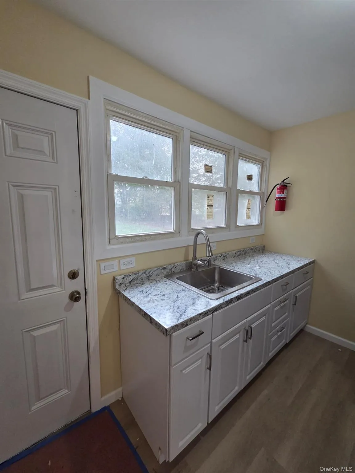 Kitchen featuring light countertops, plenty of natural light, dark wood-style flooring, and white cabinetry Kitchen featuring light countertops, plenty of natural light, dark wood-style flooring, and white cabinetry