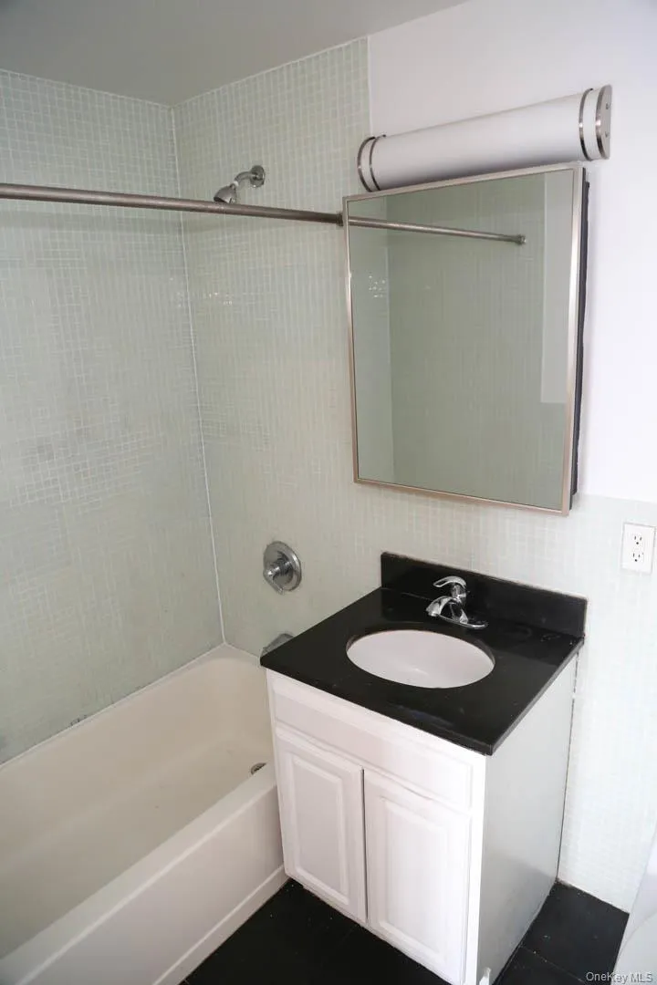 Bathroom featuring bathing tub / shower combination, vanity, and dark tile patterned flooring Bathroom featuring bathing tub / shower combination, vanity, and dark tile patterned flooring