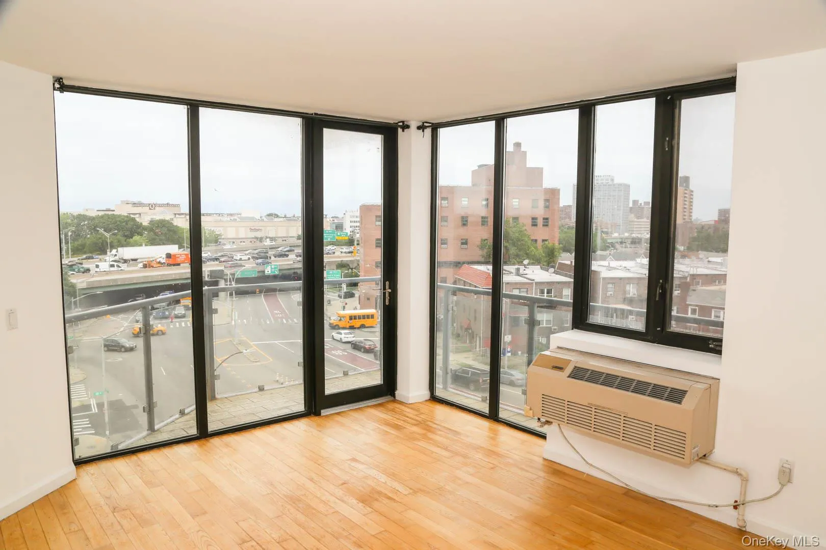 Empty room featuring expansive windows, a city view, light wood finished floors, and an AC wall unit Empty room featuring expansive windows, a city view, light wood finished floors, and an AC wall unit