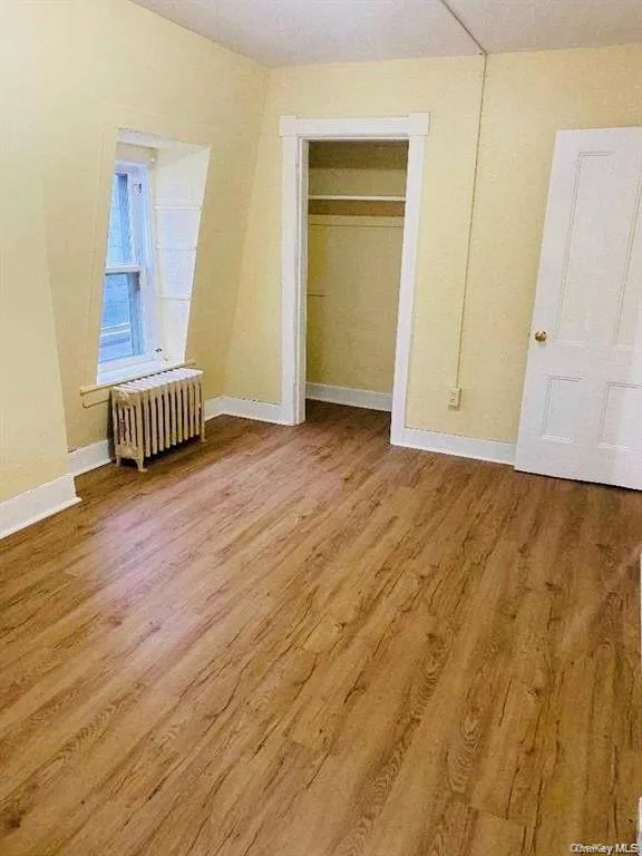 Unfurnished bedroom with a closet, radiator, and light wood-type flooring Unfurnished bedroom with a closet, radiator, and light wood-type flooring