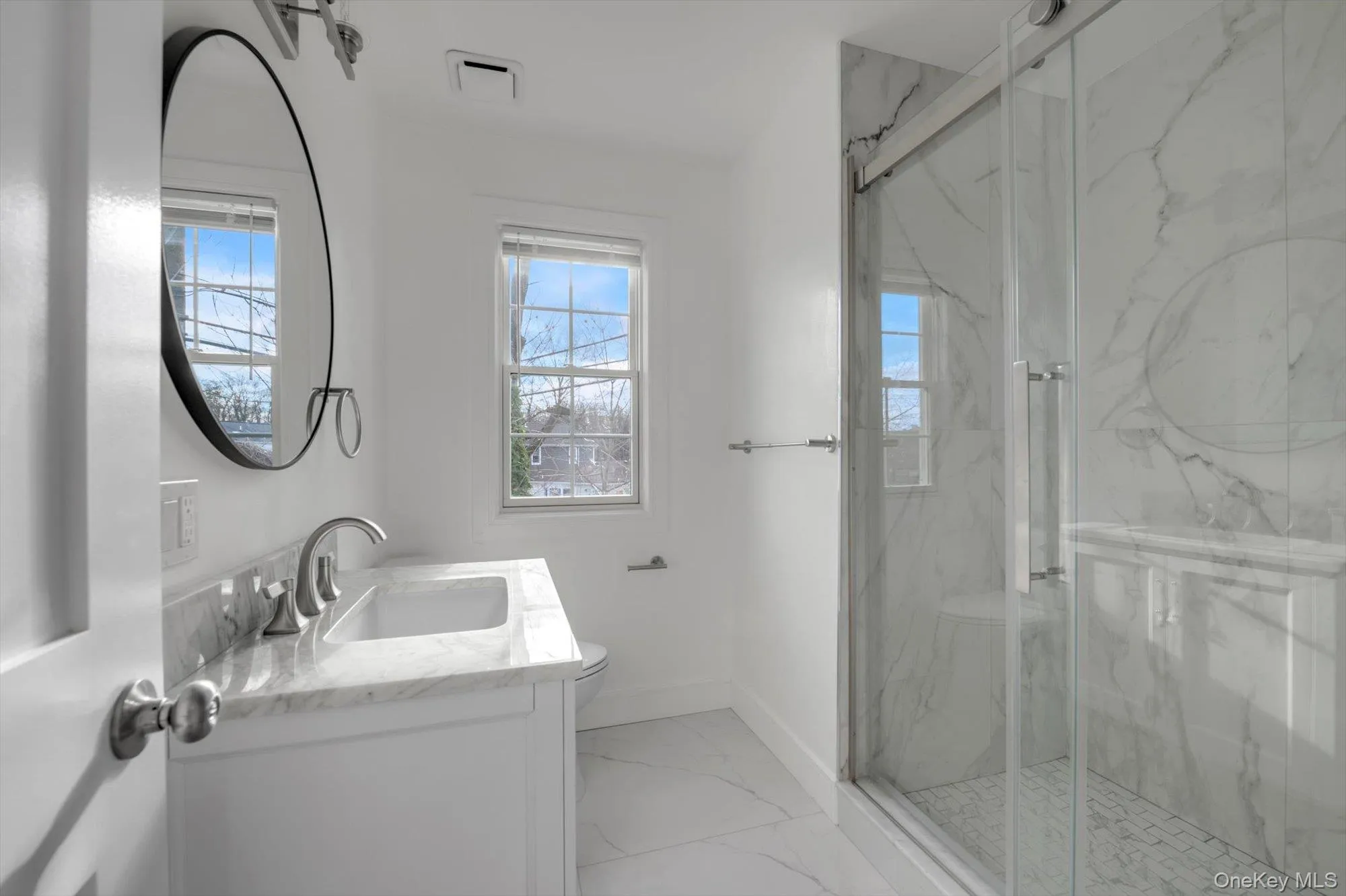Full bath featuring light marble finish flooring, vanity, and a marble finish shower Full bath featuring light marble finish flooring, vanity, and a marble finish shower