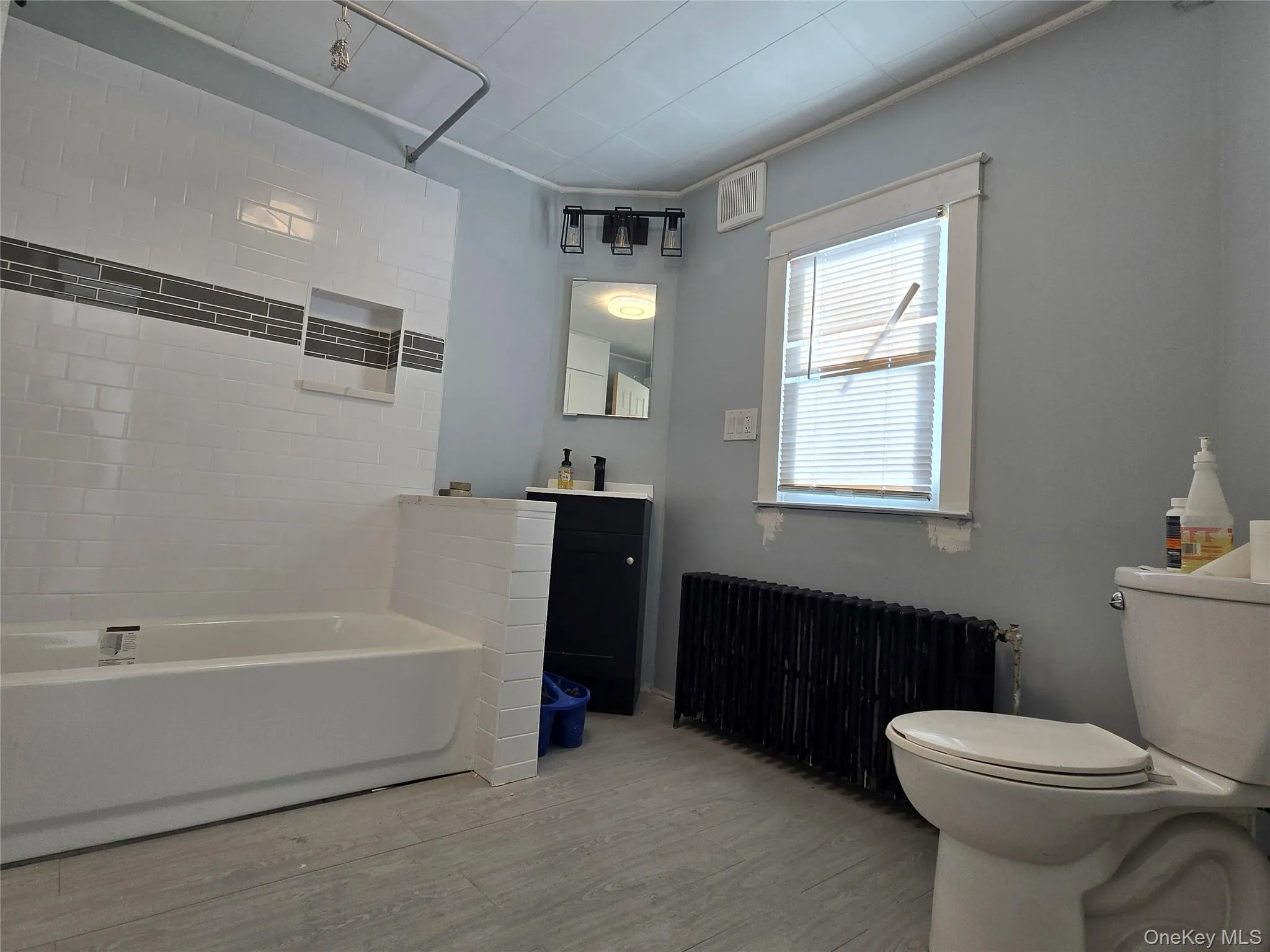 Bathroom featuring radiator heating unit, vanity, shower / washtub combination, and light wood-style flooring Bathroom featuring radiator heating unit, vanity, shower / washtub combination, and light wood-style flooring