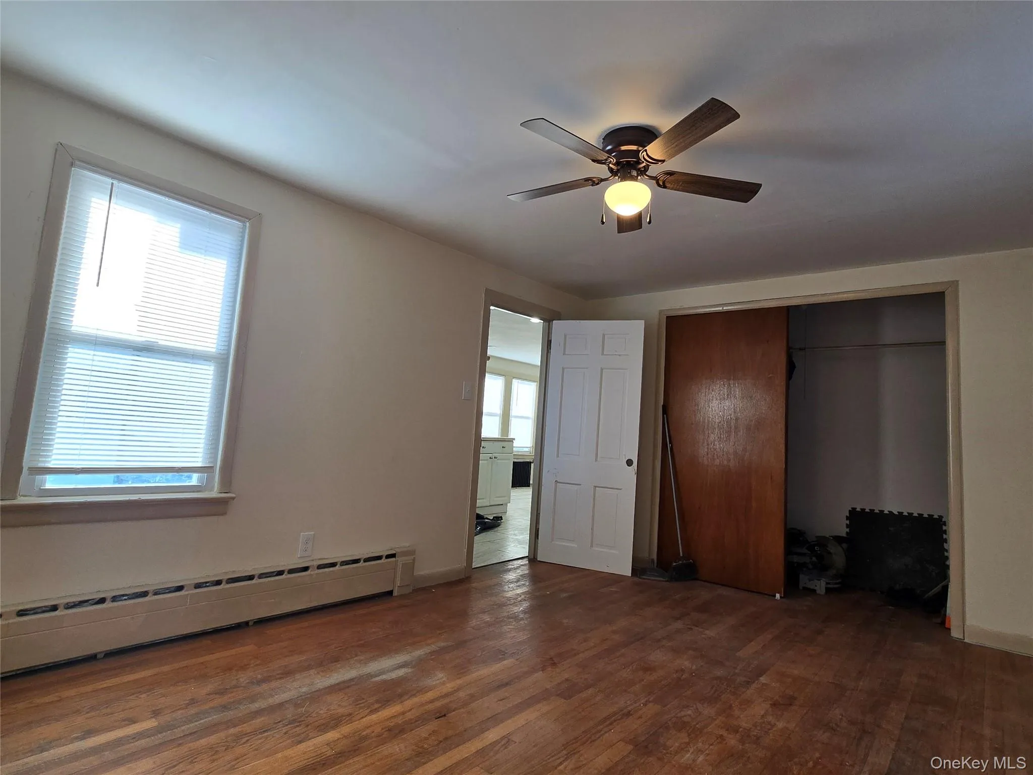 Unfurnished bedroom with a baseboard radiator, dark wood-type flooring, ceiling fan, and a closet Unfurnished bedroom with a baseboard radiator, dark wood-type flooring, ceiling fan, and a closet