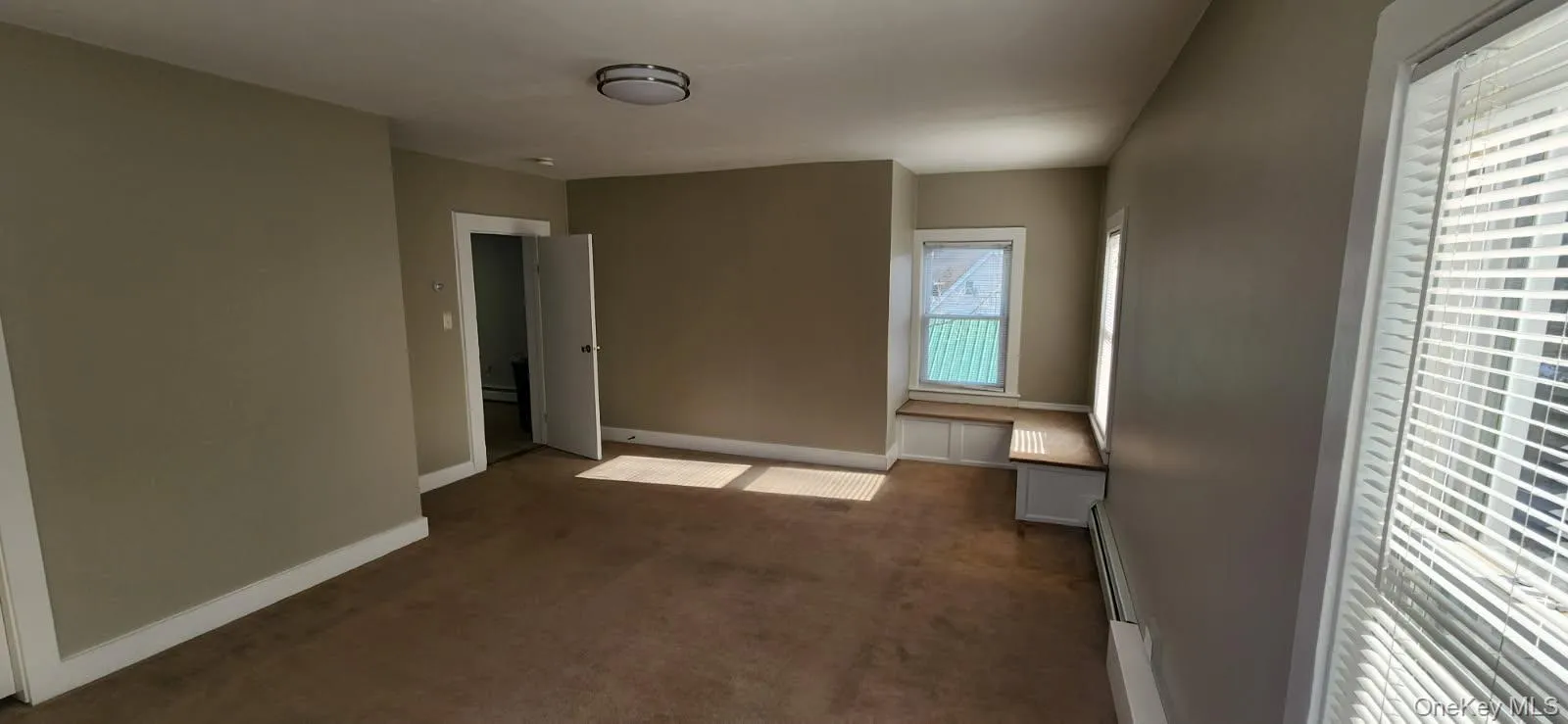 Unfurnished bedroom featuring dark colored carpet and a baseboard radiator Unfurnished bedroom featuring dark colored carpet and a baseboard radiator