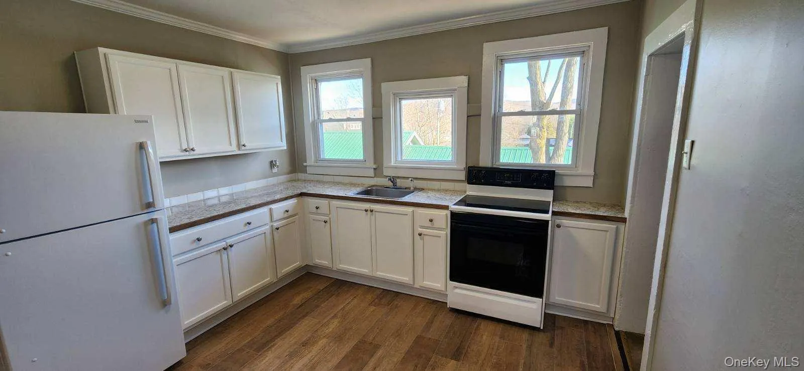 Kitchen featuring freestanding refrigerator, white cabinets, electric range oven, dark wood-type flooring, and ornamental molding Kitchen featuring freestanding refrigerator, white cabinets, electric range oven, dark wood-type flooring, and ornamental molding