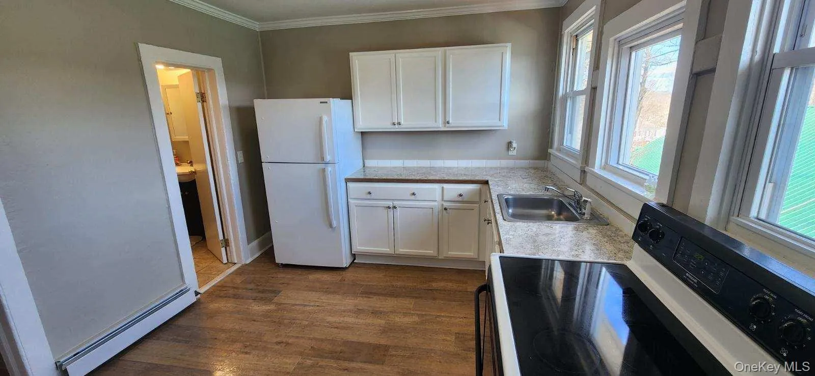 Kitchen with electric range, white cabinetry, light countertops, a baseboard radiator, and crown molding Kitchen with electric range, white cabinetry, light countertops, a baseboard radiator, and crown molding